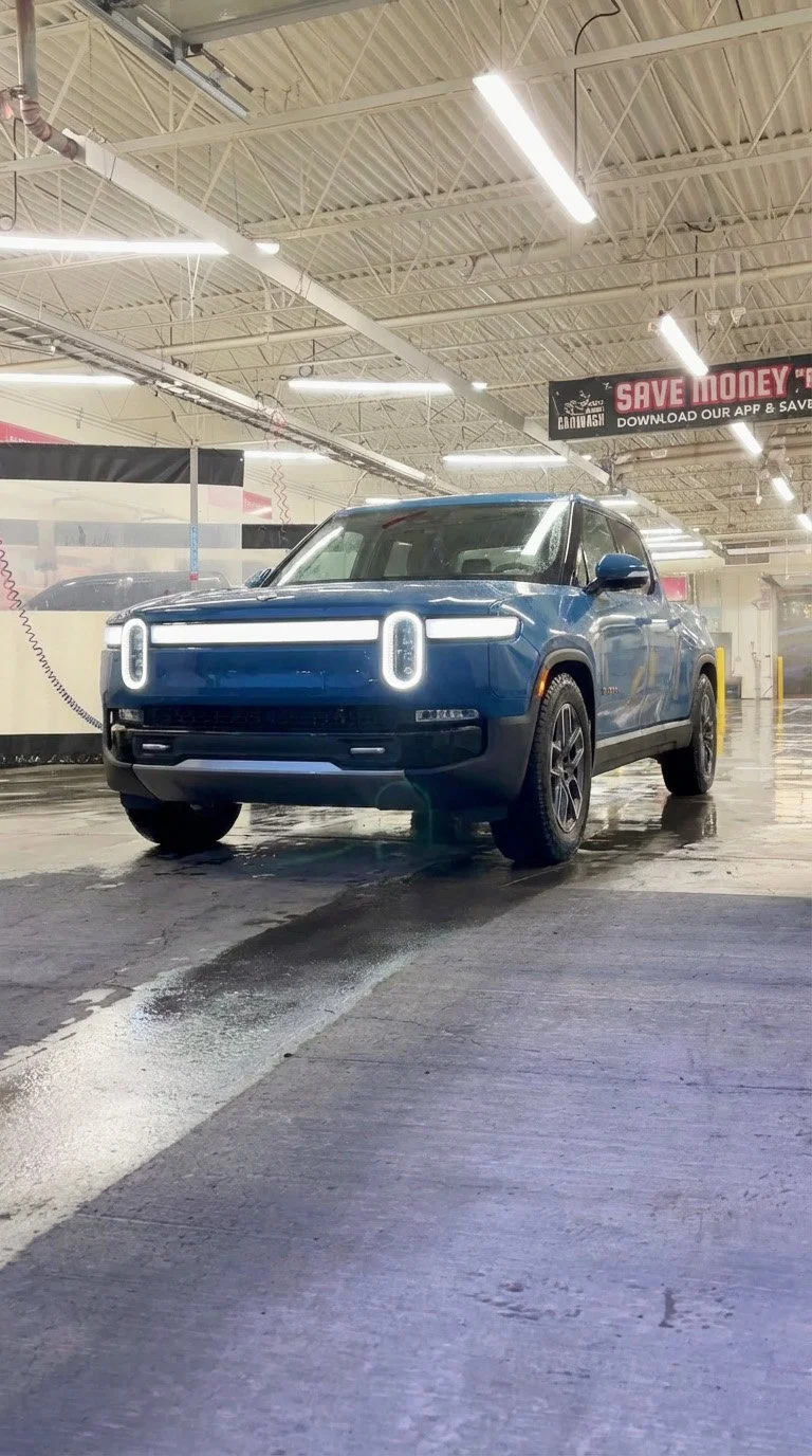A blue electric SUV is parked inside a car wash with foam and water on the ground.