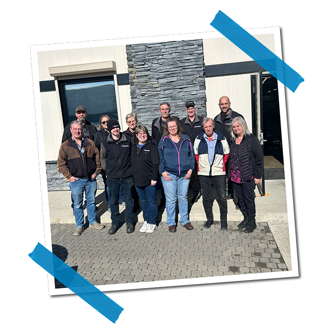 A group of eleven people standing outside a building with stone and white siding, smiling for a photo.