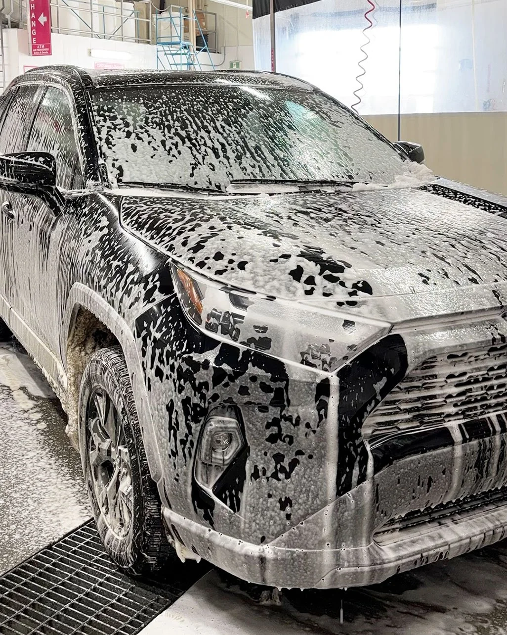 A black SUV covered in soap bubbles during a car wash at a facility.
