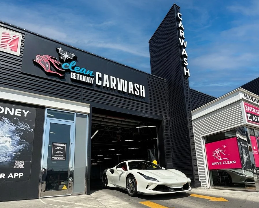 A white sports car parked inside a car wash facility with the sign 'Clean Getaway Car Wash' on the building.