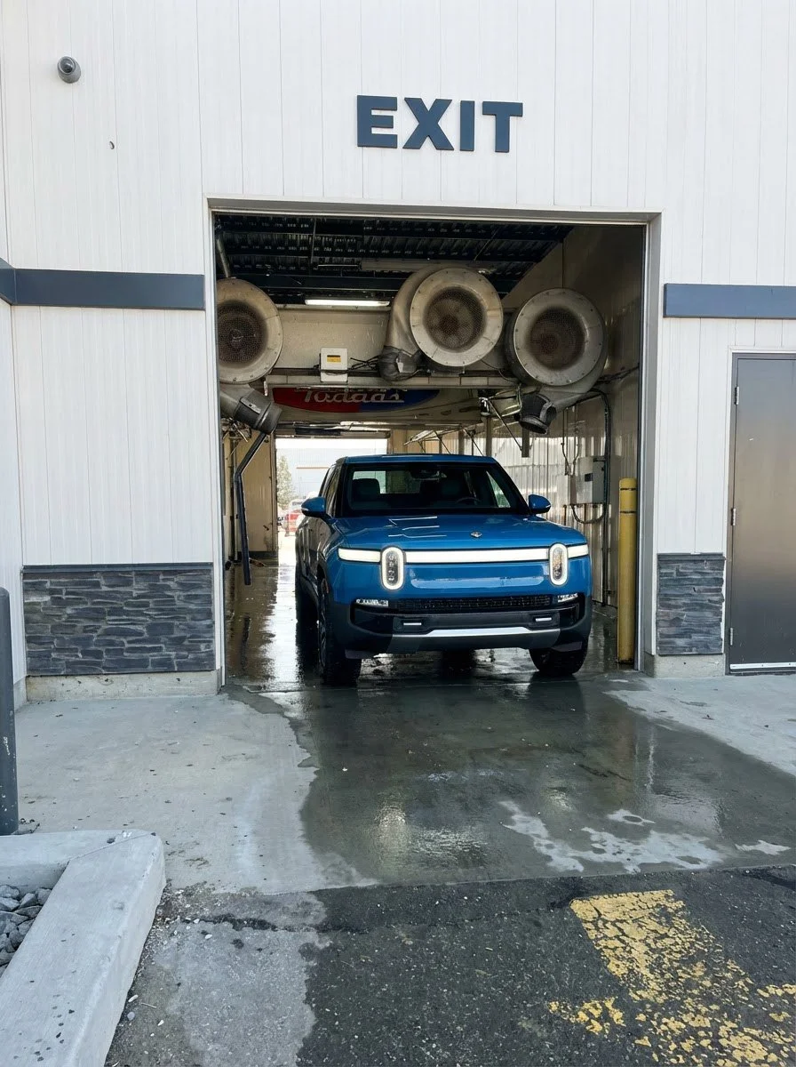 A blue vehicle is being washed inside an automatic car wash bay with a large sign reading 'EXIT' above the entrance.
