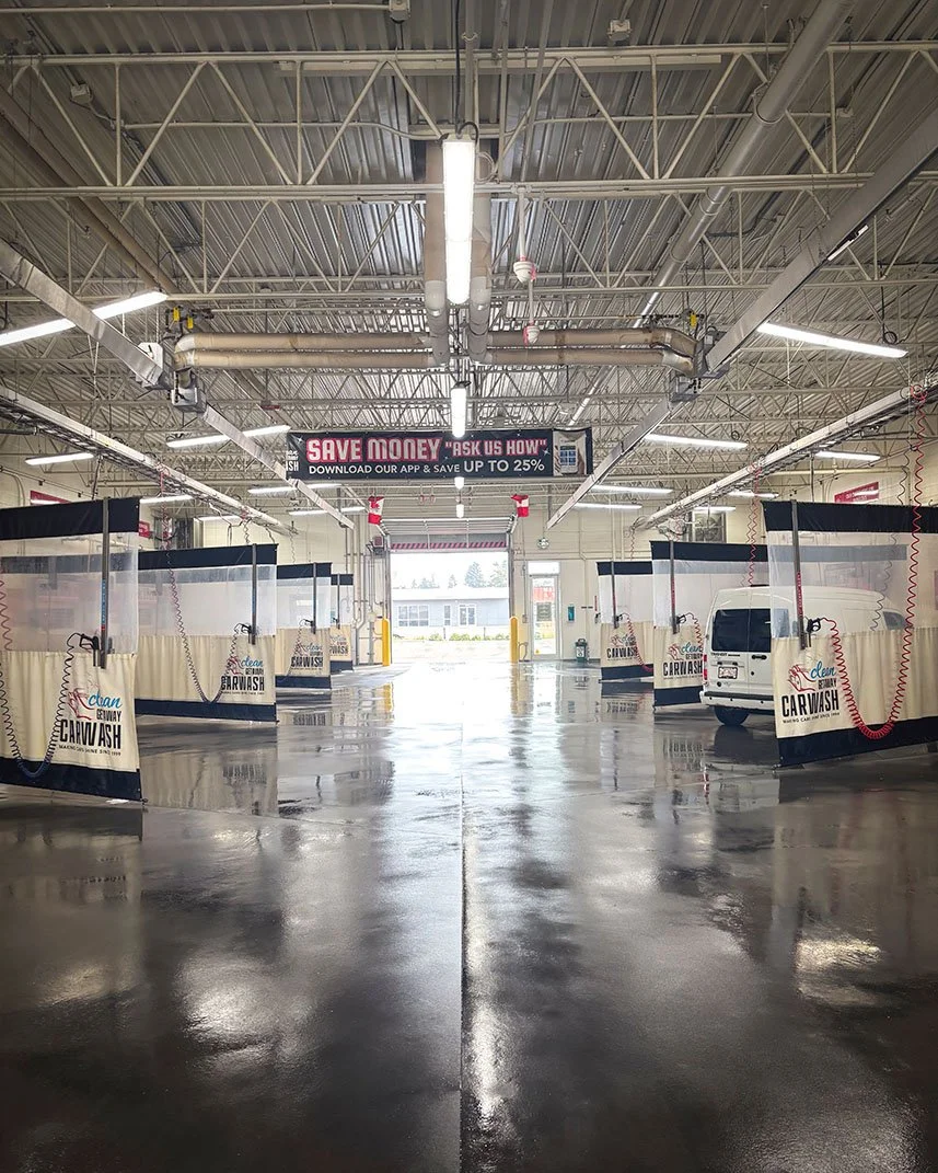 Empty automatic car wash bays inside a spacious garage with curved hose reels and a van in the background