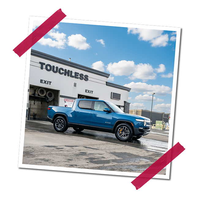 A blue pickup truck parked outside a building with a sign that says 'TOUCHLESS' under a partly cloudy sky.