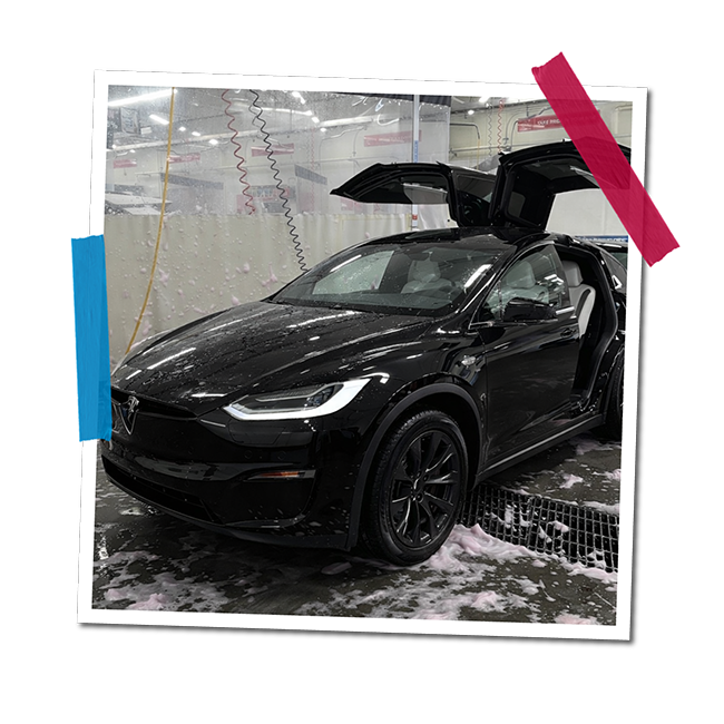 Black electric SUV with open gullwing doors being washed in an automatic car wash