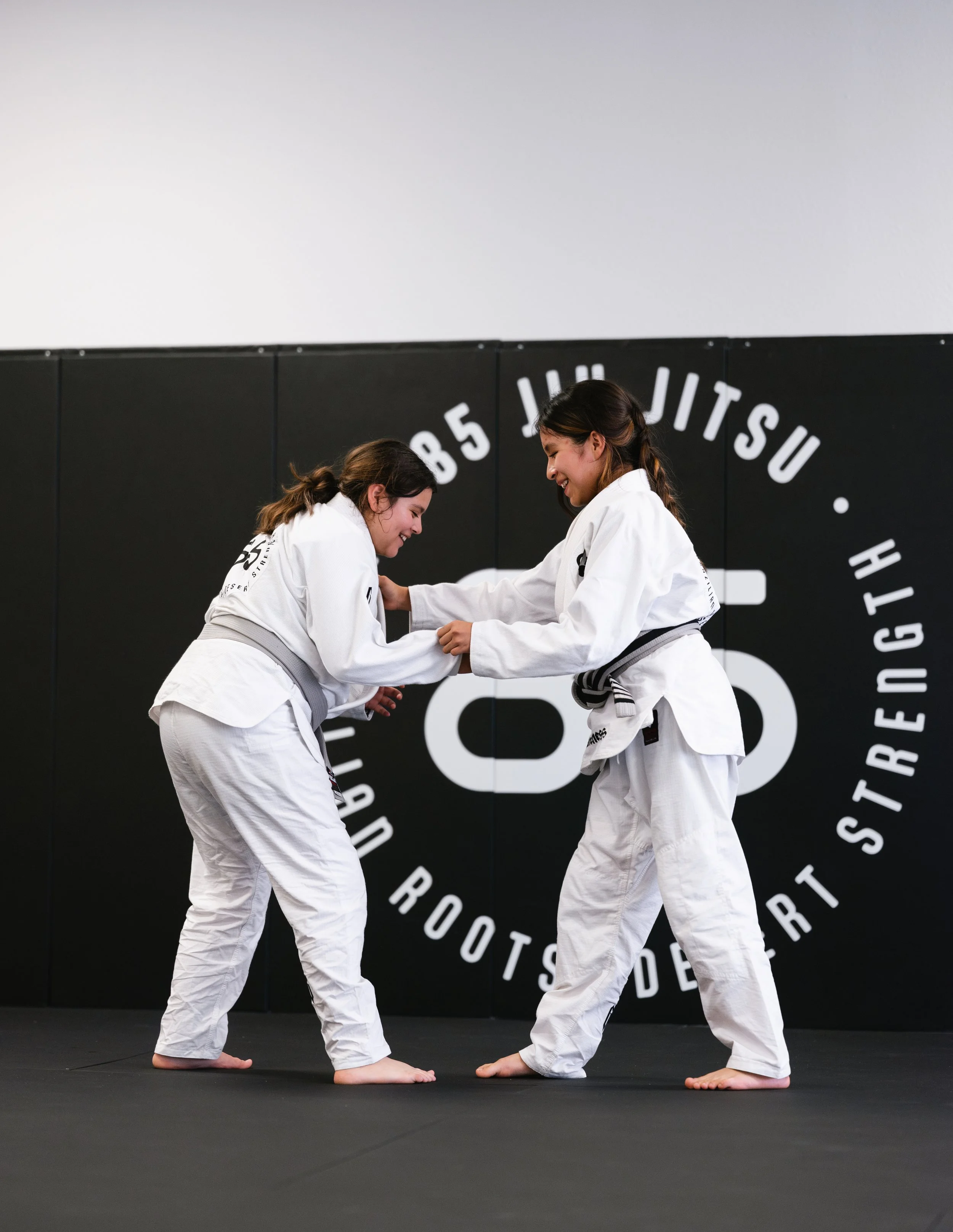 Two children practicing Brazilian Jiu-Jitsu on a mat, one on top and the other on the bottom, in a training session.