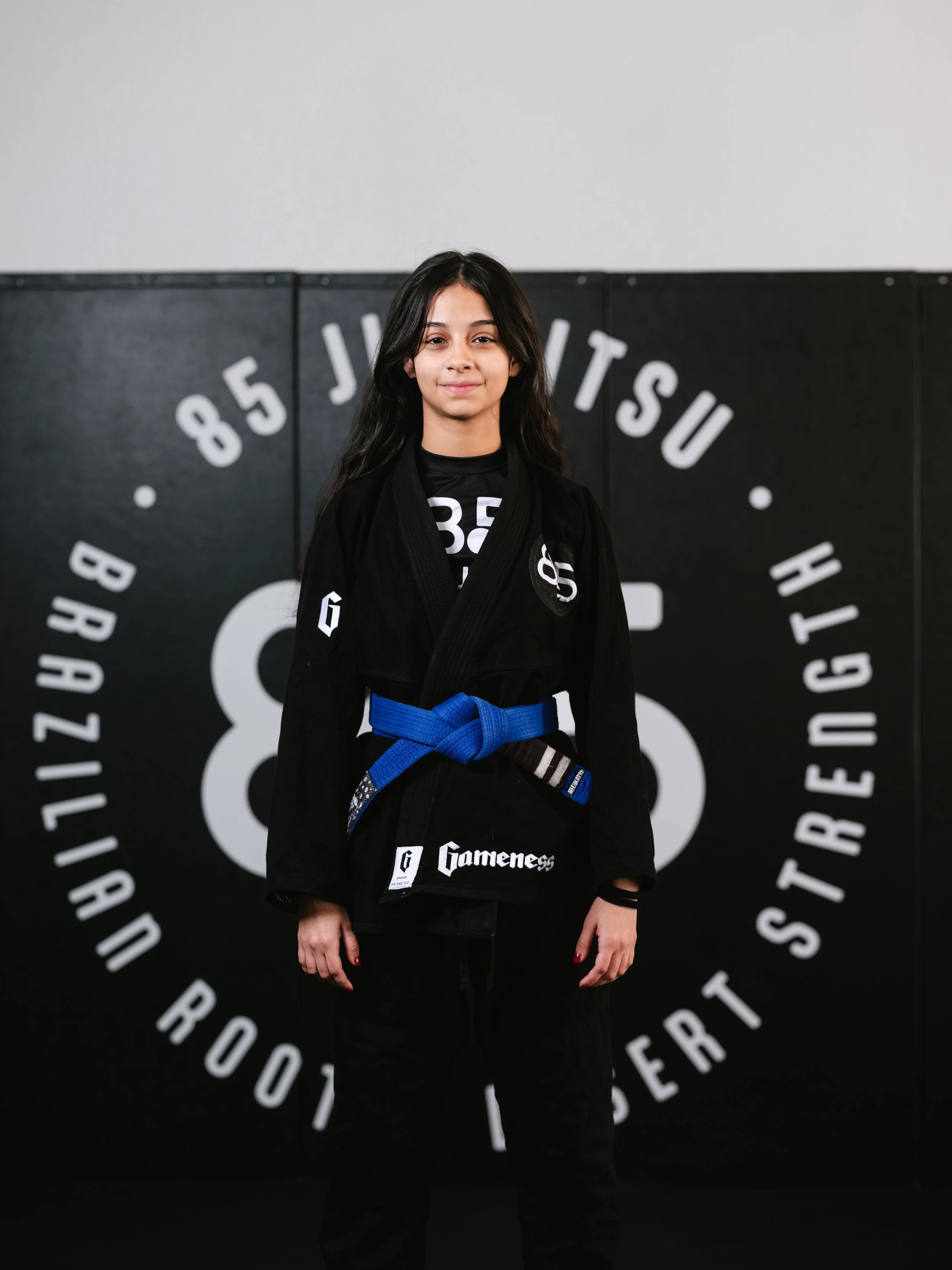A young girl in a martial arts uniform standing in front of a black background with circular white text.