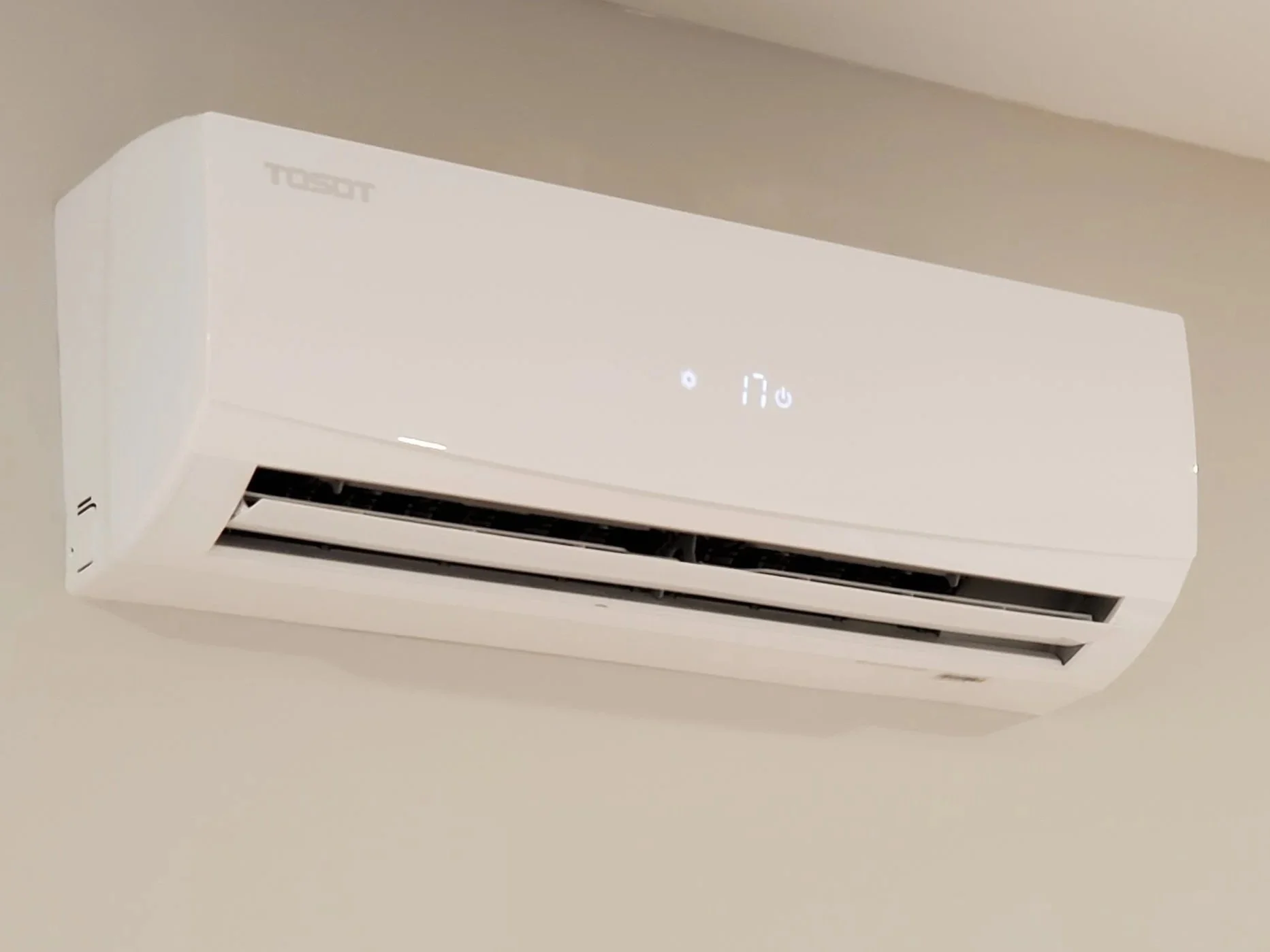 White wall-mounted TOSOT heat pump with digital display showing temperature, installed on a ceiling.