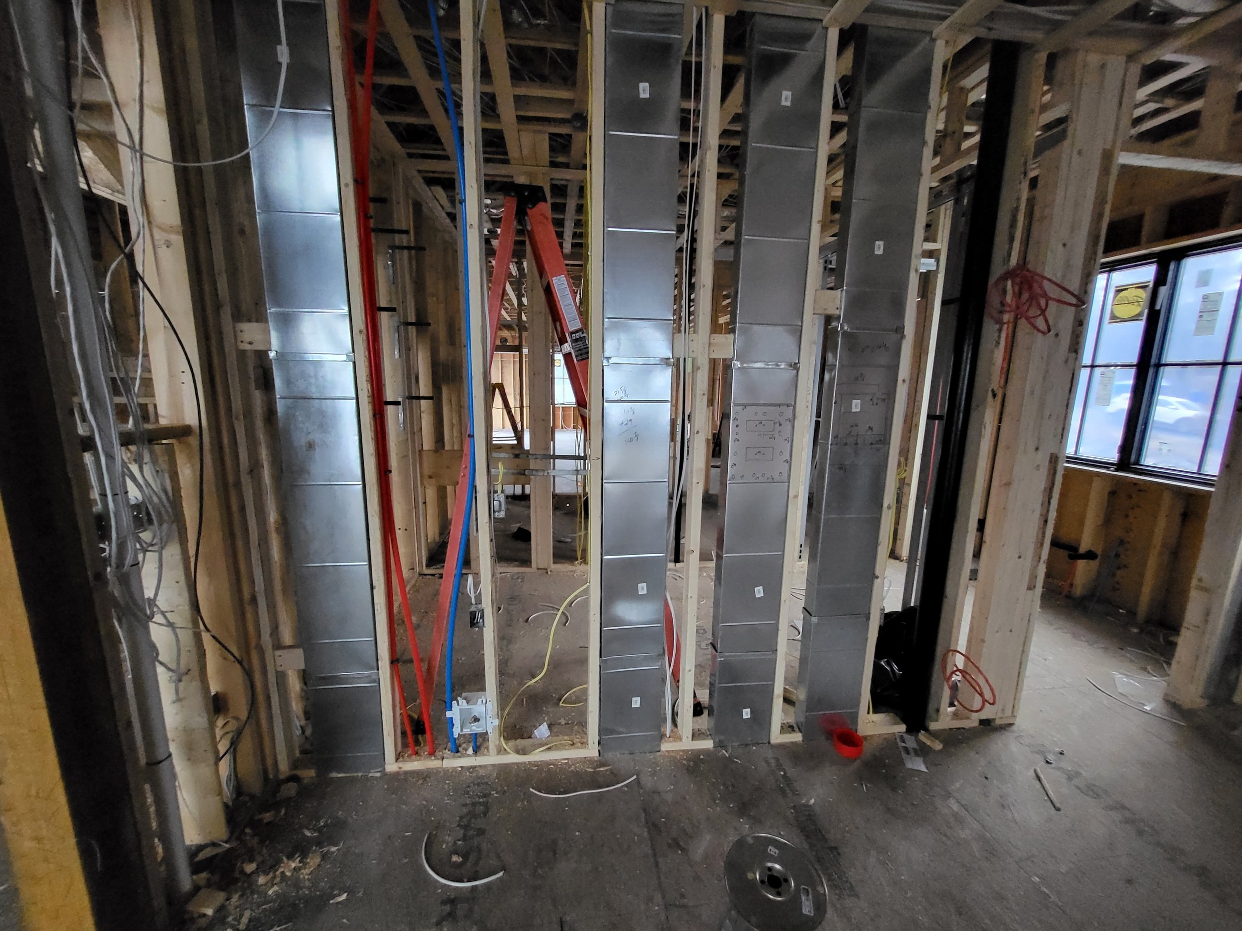 Interior of a home under construction during renovation showing exposed wooden framing, metal electrical boxes, and electrical conduit, with windows on the right side.