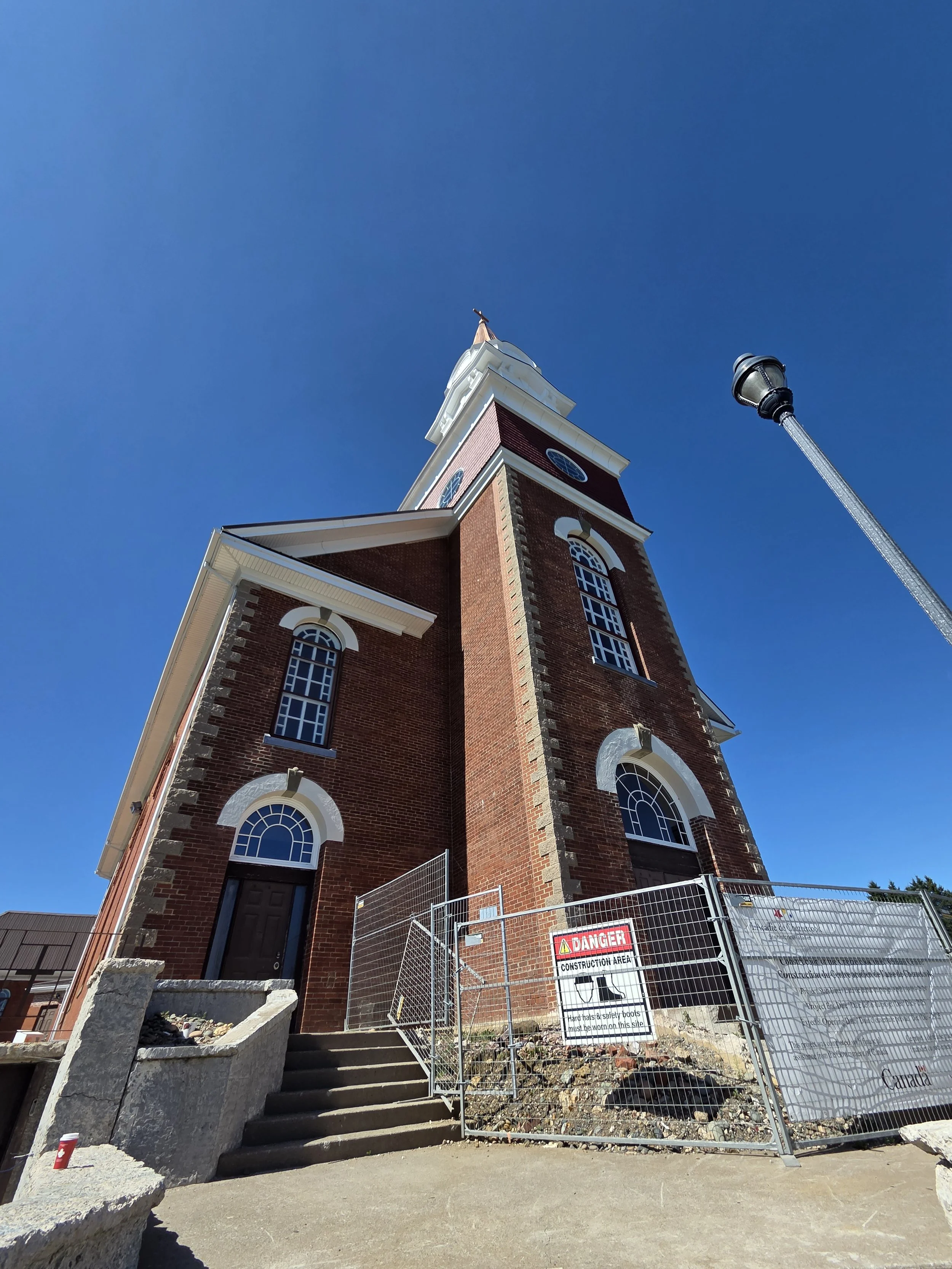 A tall brick church steeple under a clear blue sky, with a construction fence. Commercial ventilation, HVAC, Nova Scotia 