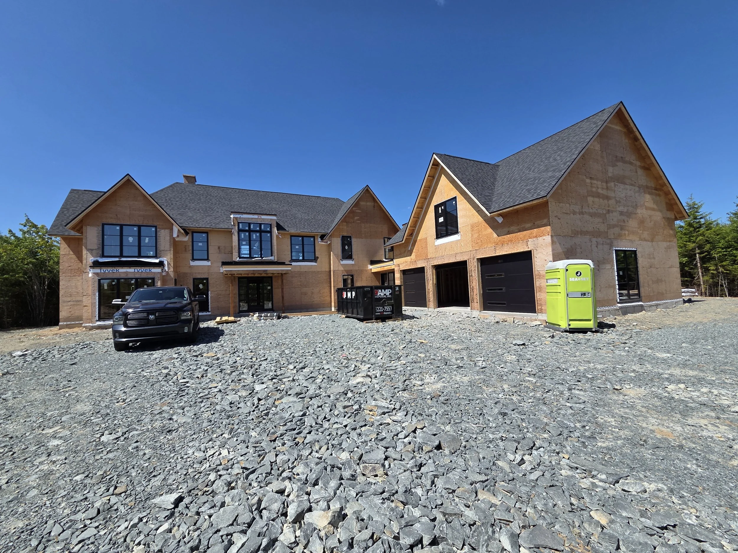 Large house under construction with a black car parked in front, gravel driveway, new construction. Ventilation, ducted heat pump