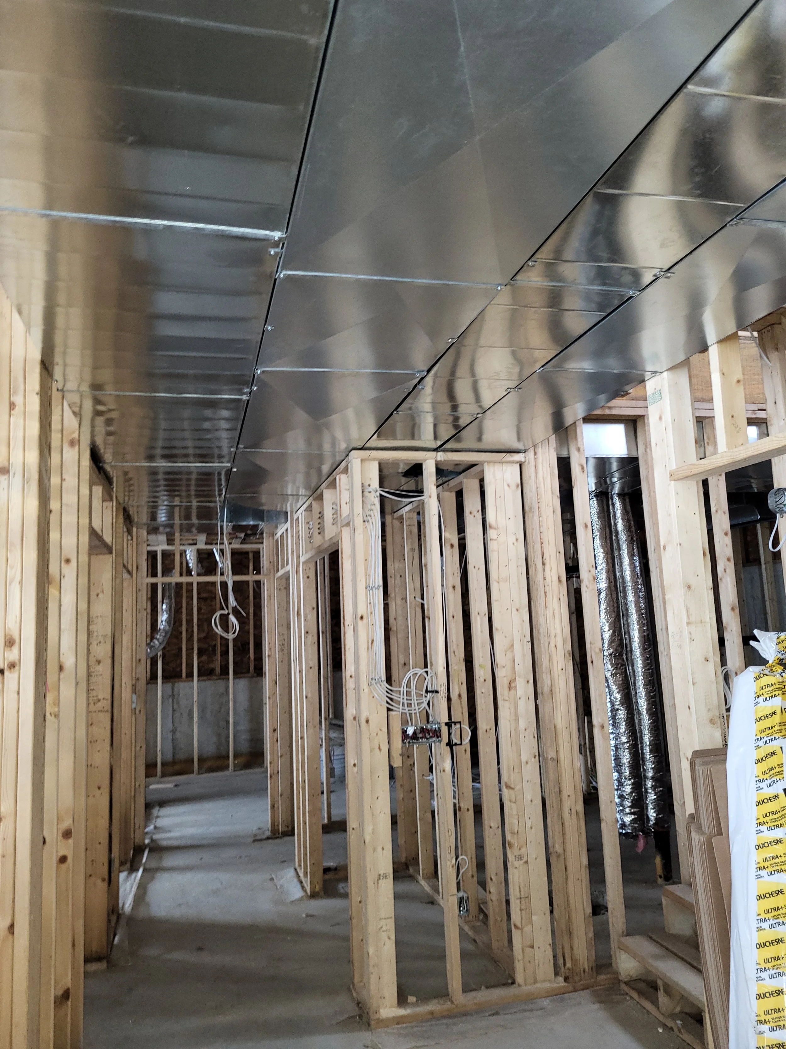 Construction site with exposed wooden framing and metallic ductwork installed in the ceiling. 