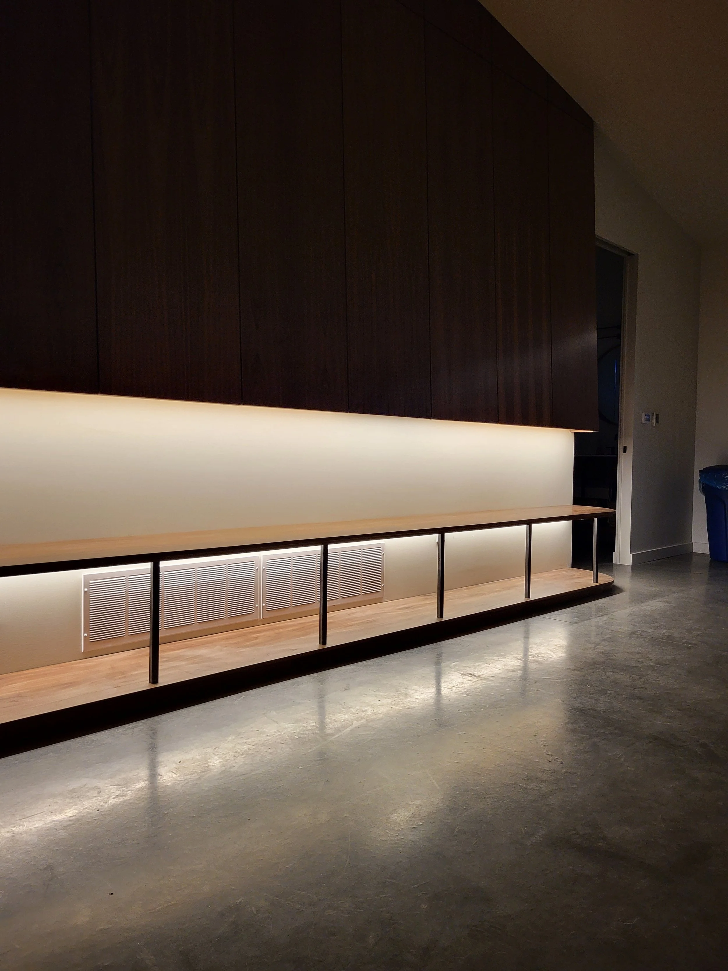 Modern interior with a long wooden bench, dark wooden cabinets above, wall-mounted lighting, and polished concrete floor. home ventilation, ductwork