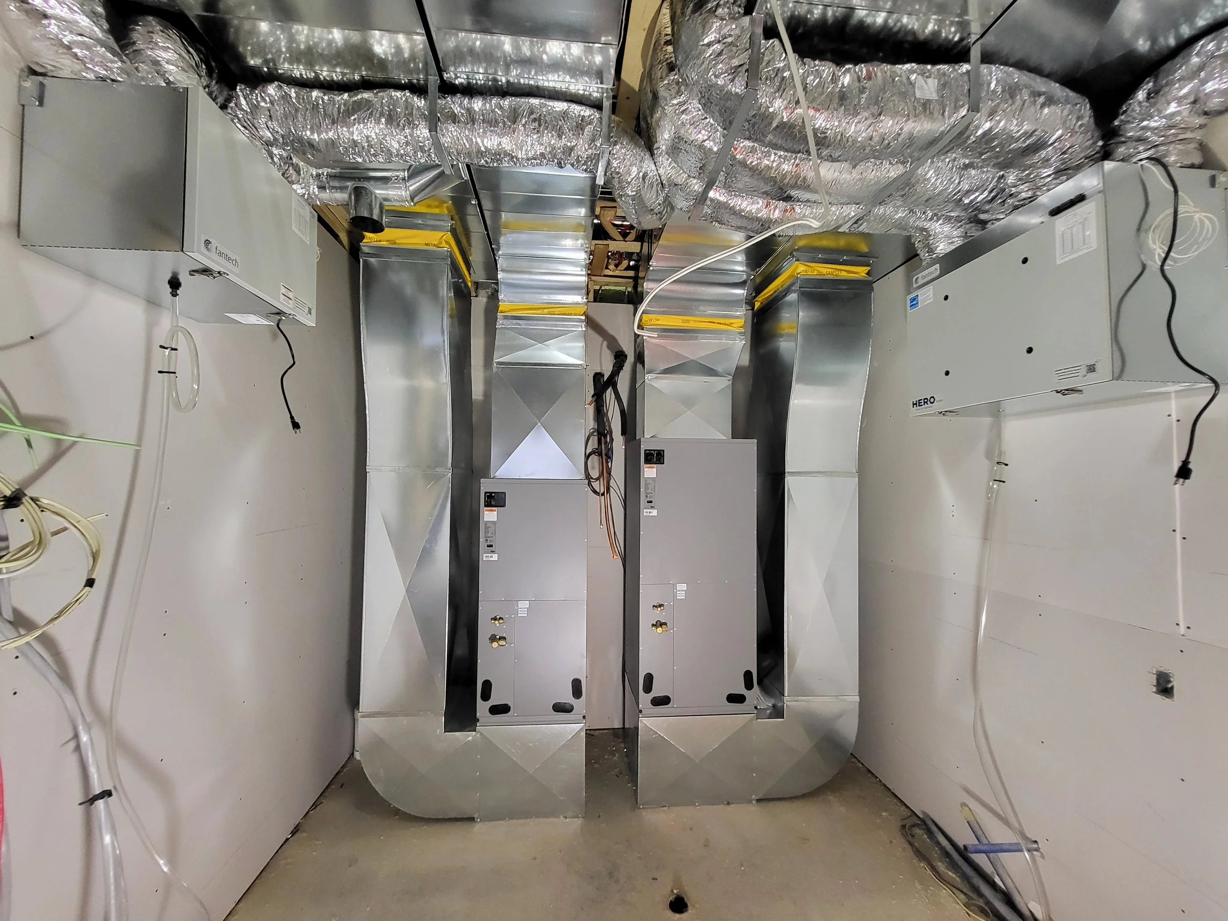 A view of an industrial HVAC system with metal ducts and equipment installed in a utility or mechanical room. ducted heat pump