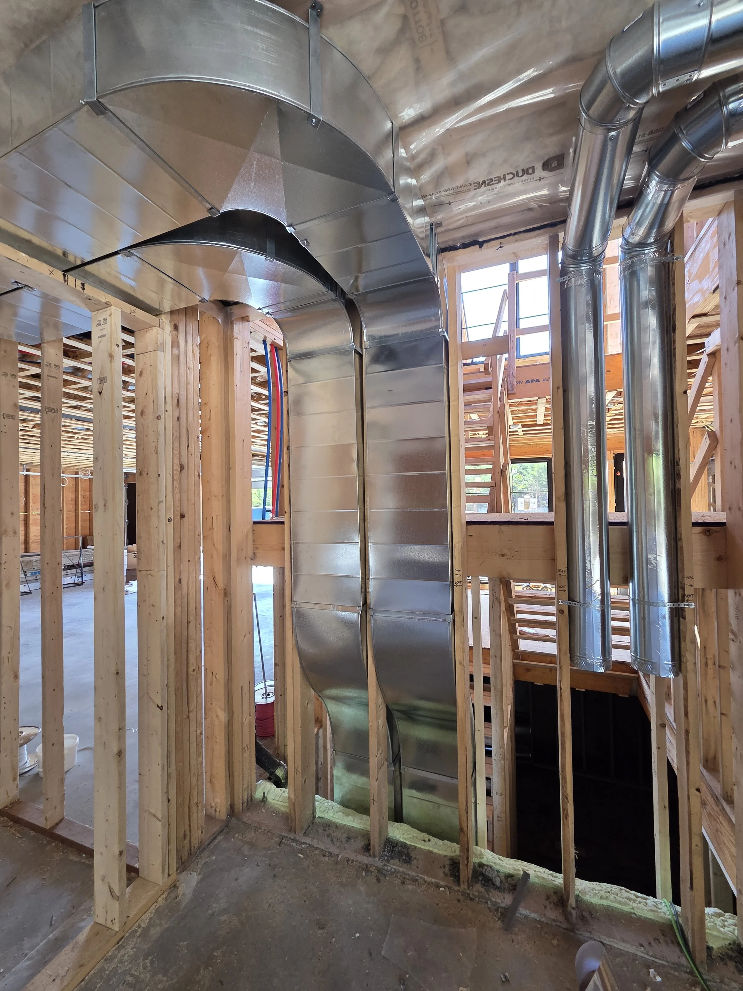 Metal HVAC ducts installed in a wood-framed building under construction.