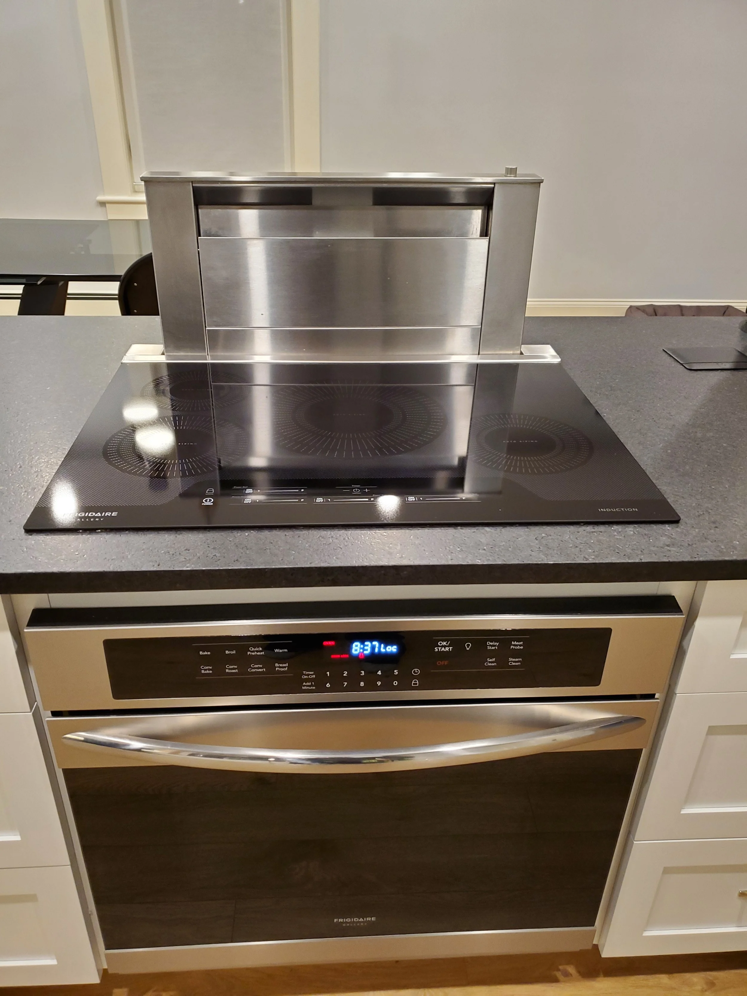 A modern kitchen with a black ceramic electric cooktop and a stainless steel oven underneath, set into a black countertop with white cabinets on the sides. kitchen range