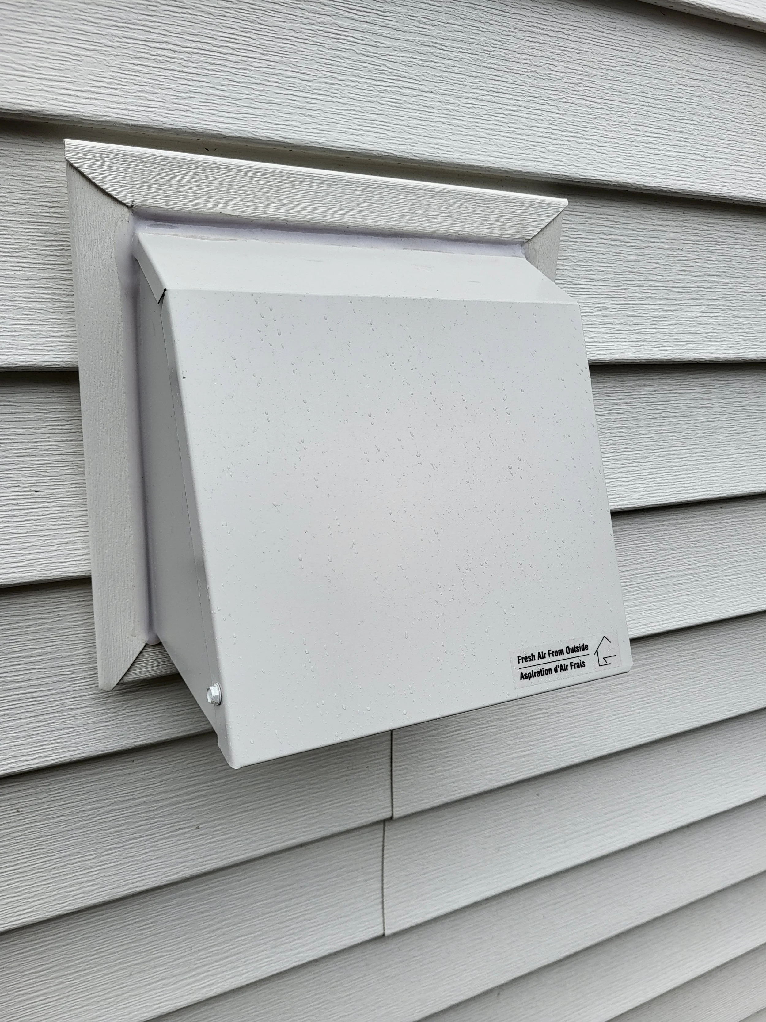 White vent  mounted on the exterior of a beige siding house, allowing fresh air intake from outside and quality air flow.