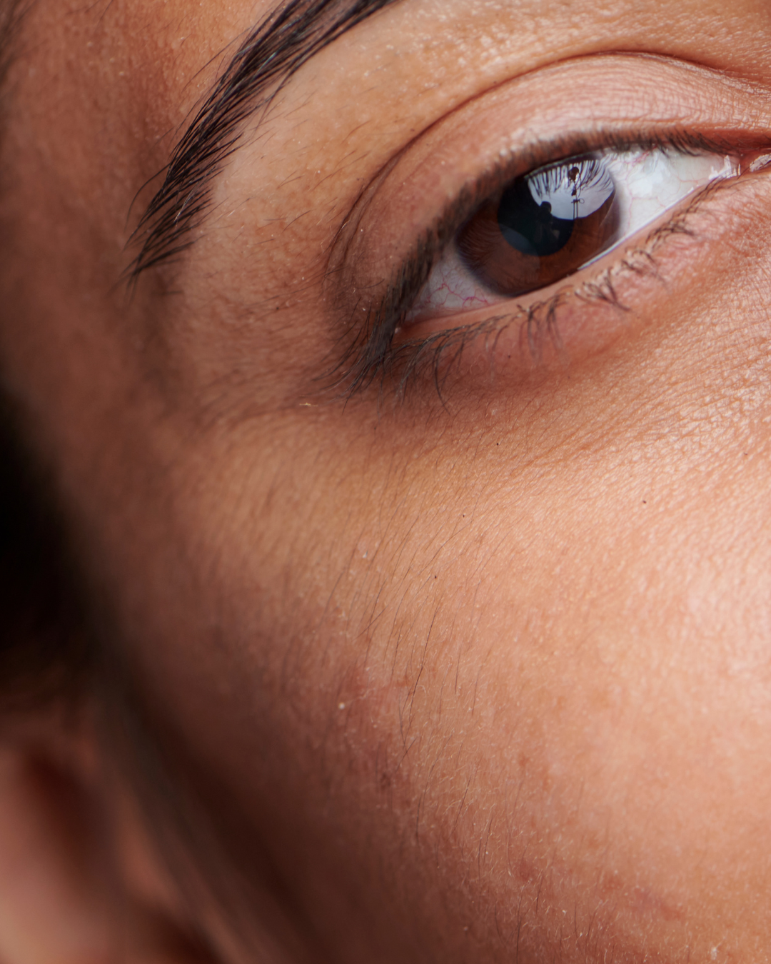 Close-up of a brown eye and surrounding skin with detailed eyelashes and skin texture.