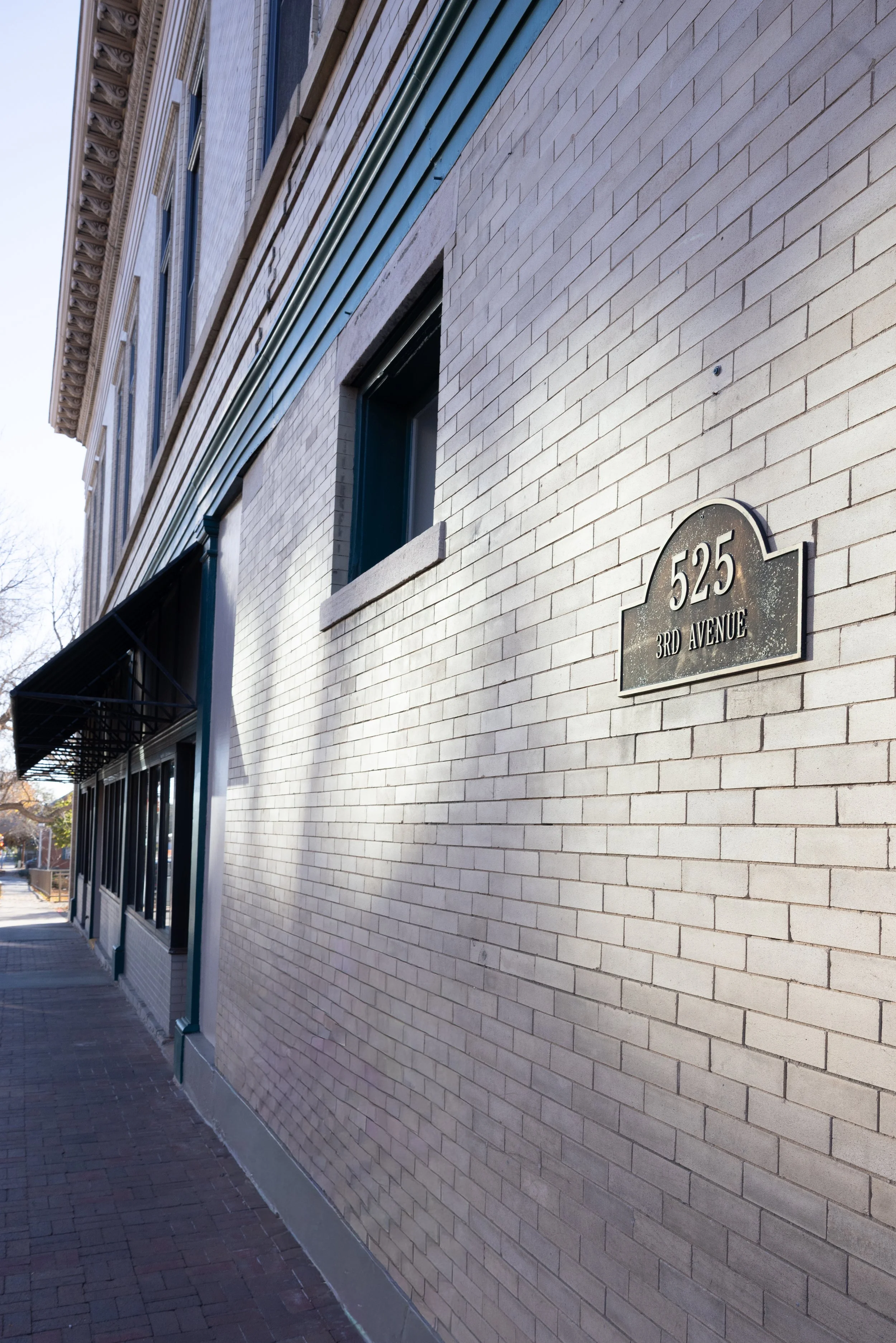A brick building with a sign that reads "525 3rd Avenue" and blue trim along the roofline, with a sidewalk in front.