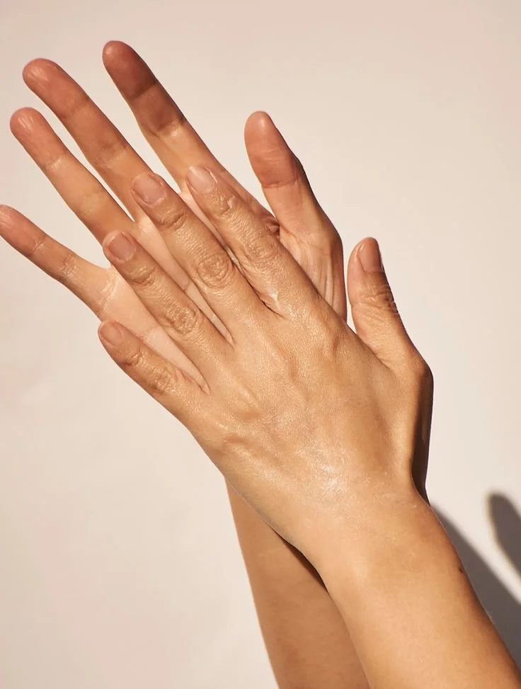 Two hands with intertwined fingers, showing a close-up of the palms and nails against a plain background.