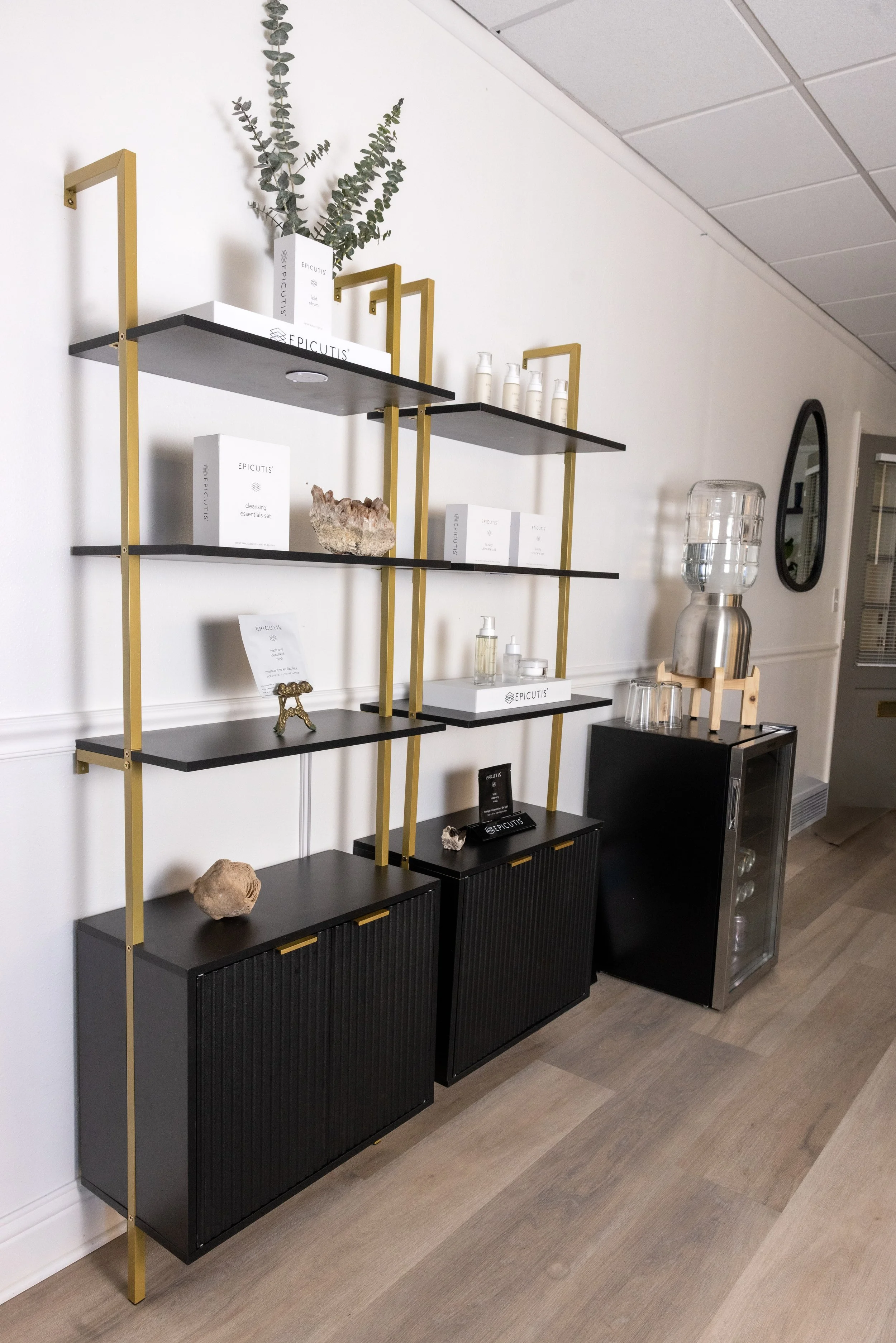 Display shelf with skincare products and decorative items next to a water dispenser, in a modern interior setting.