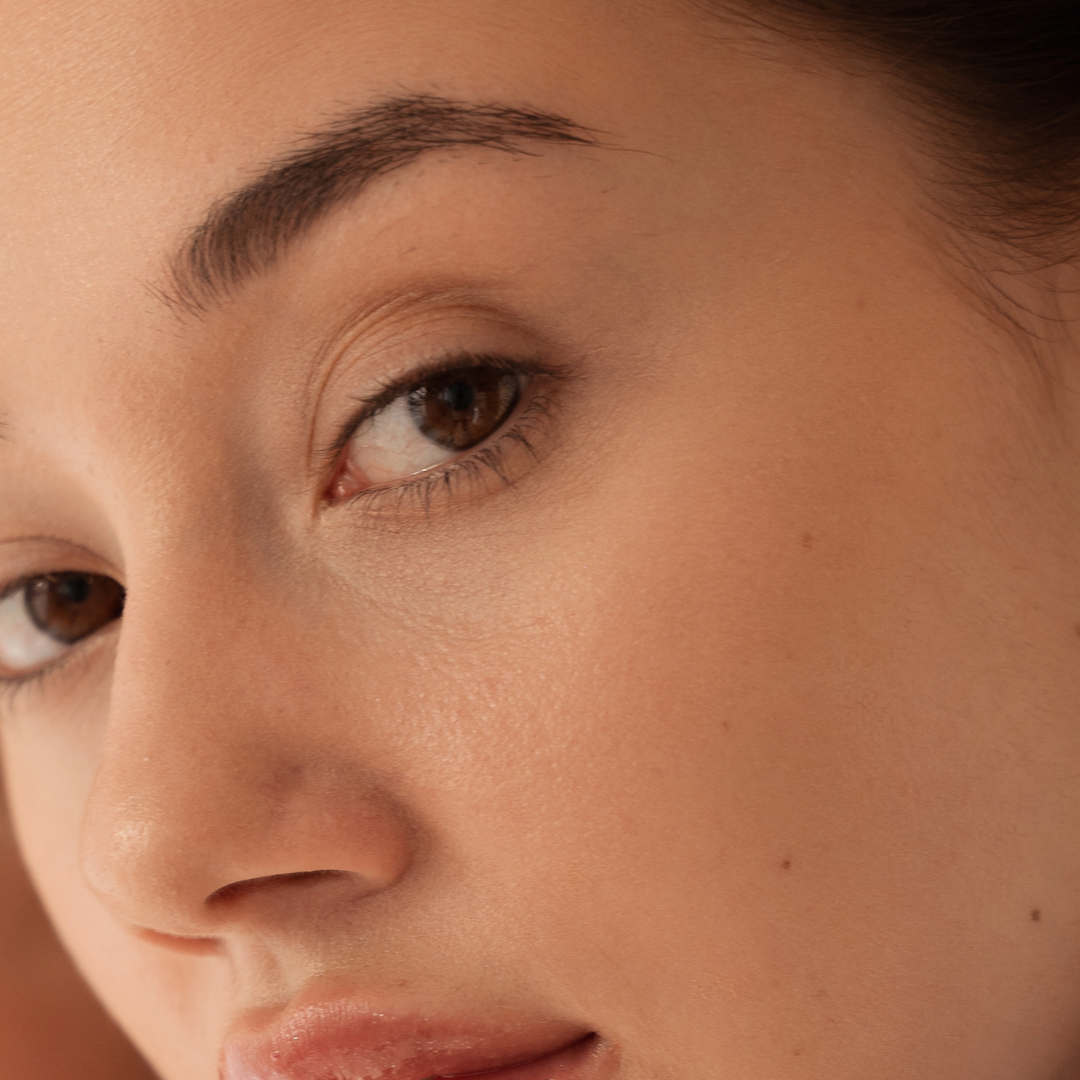 Close-up of a woman's face showing her eye, eyebrow, and part of her nose and lips with clear skin.