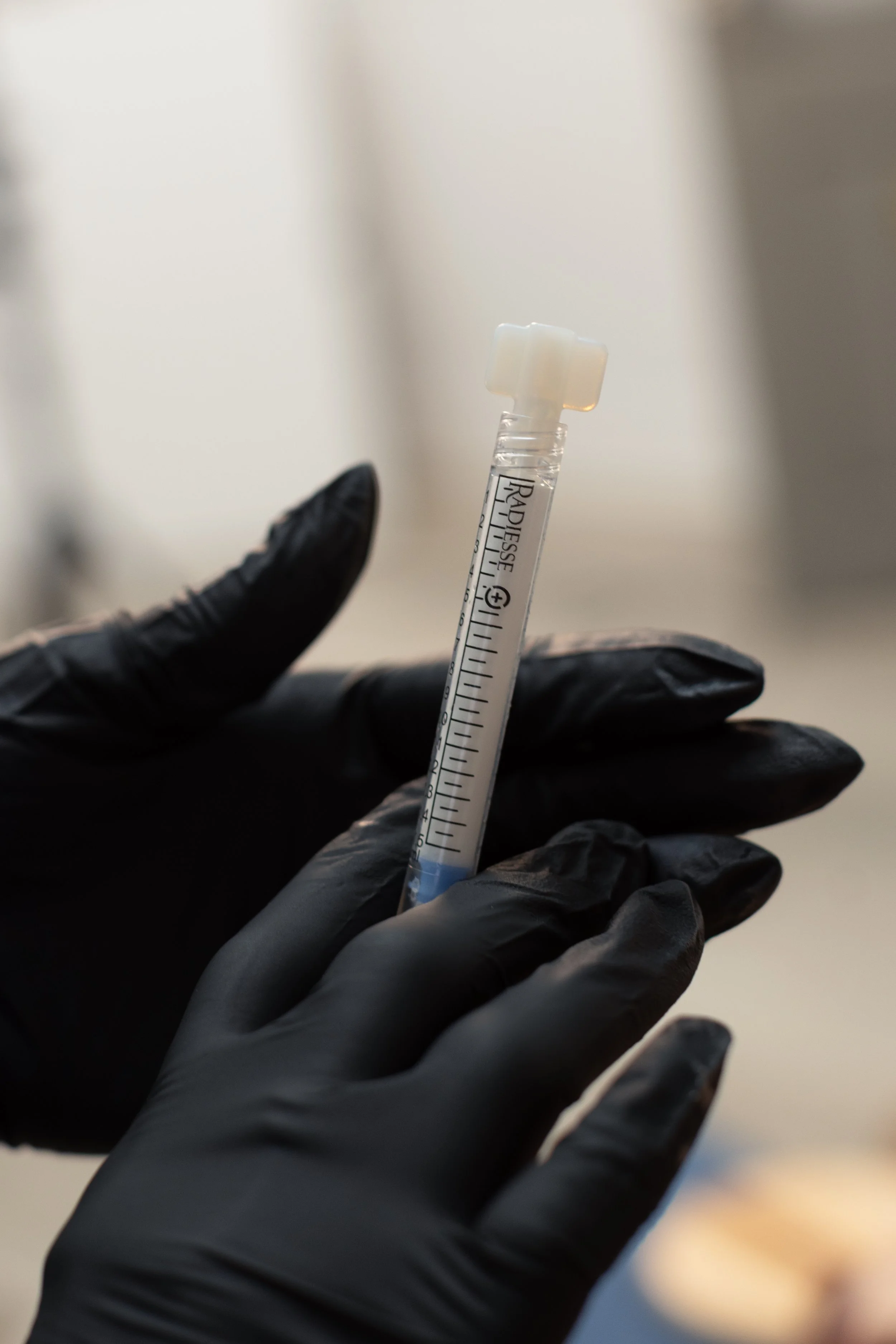 A gloved hand holding a syringe with a clear liquid.