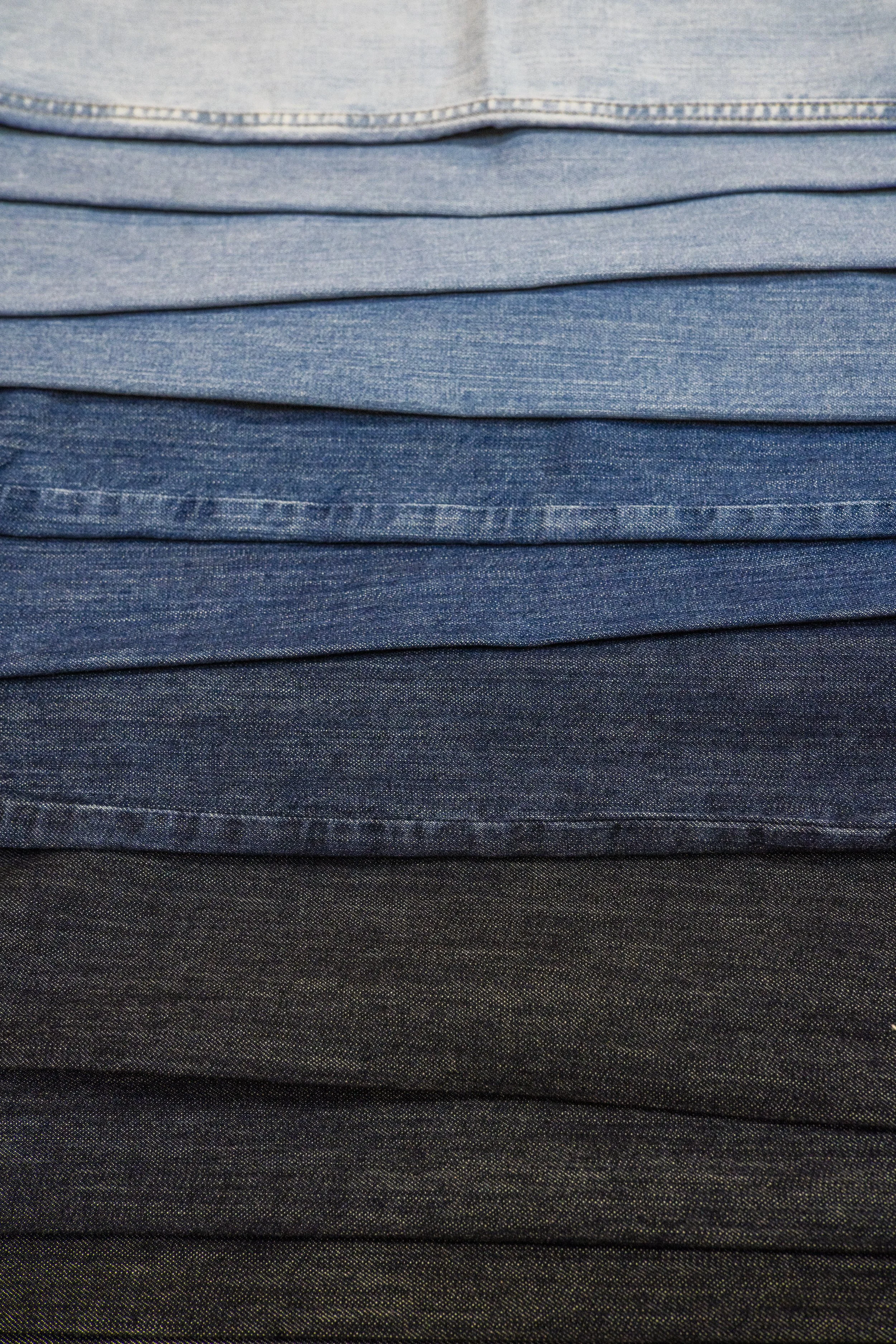 Stacked denim fabric in various shades of blue from light to dark.
