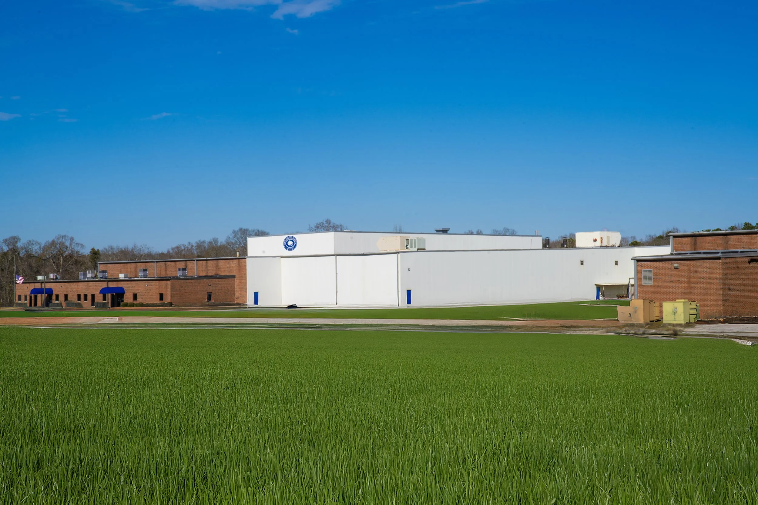 A single-story brick building with white and brown sections, blue awnings over windows, and a lawn in front under a clear blue sky.