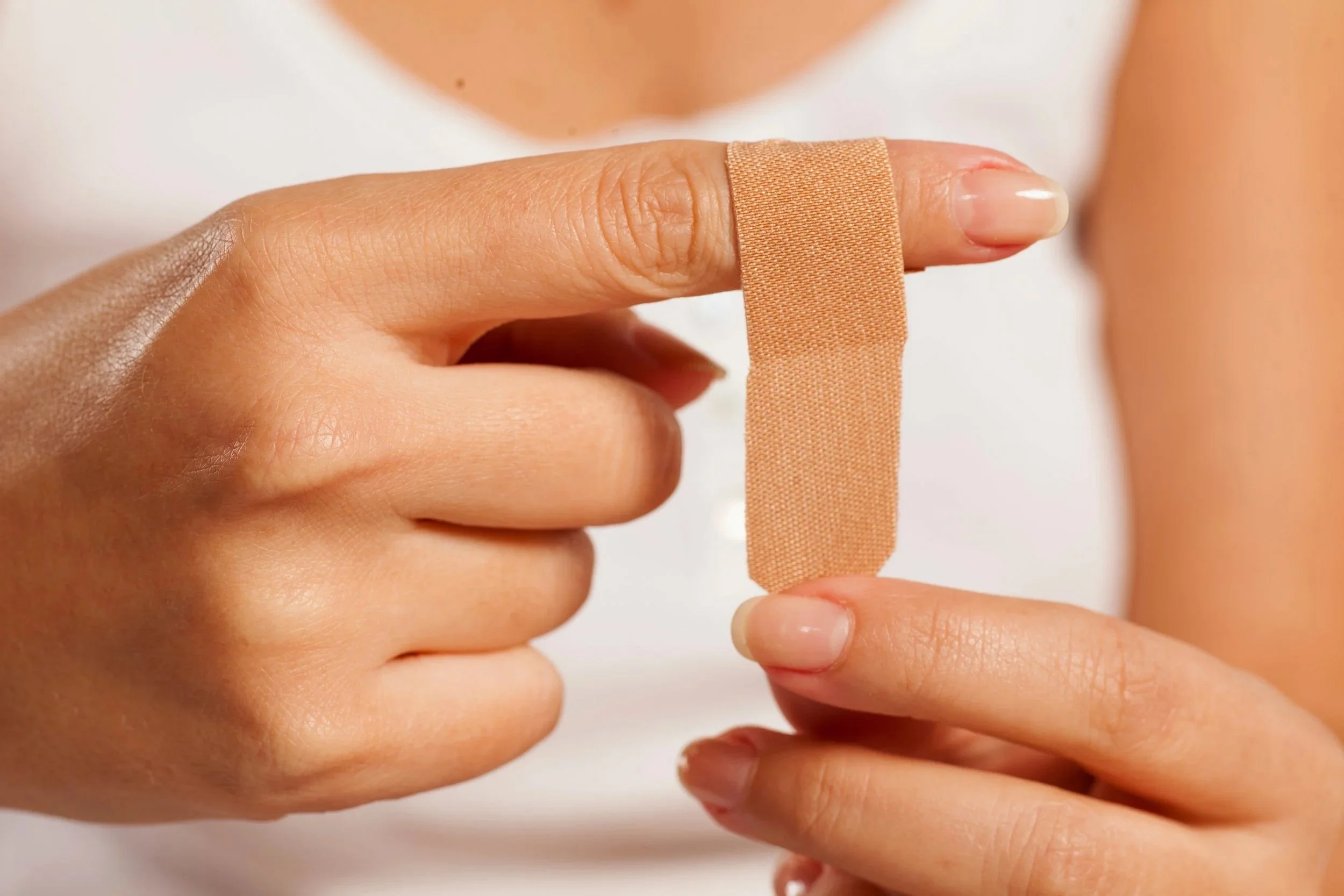 Close-up of a person's fingers holding a strip of beige adhesive medical tape.