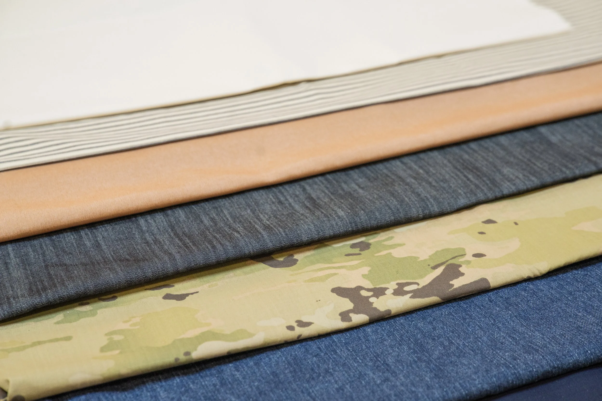 Stack of fabric pieces in various colors and patterns, including solid dark blue, solid peach, and camouflage design, on a table.
