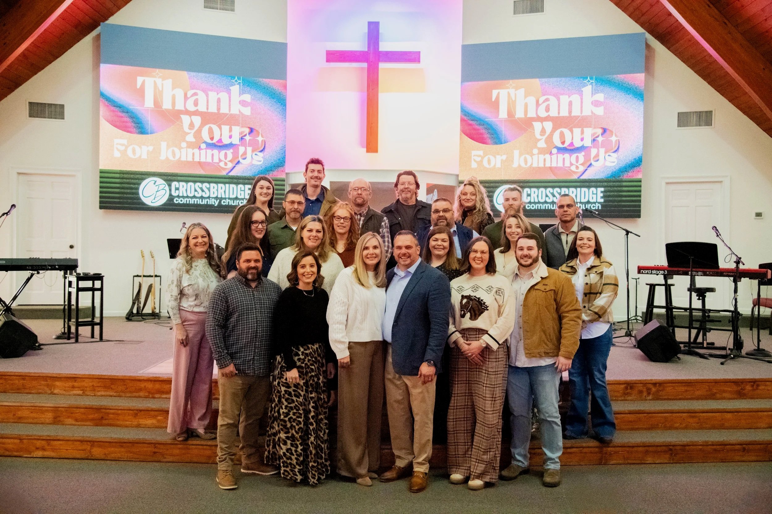 A group of people standing on stage inside a church, with a large screen behind them displaying a message thanking attendees, and the church's name, Crossbridge Community Church, along with a cross symbol.
