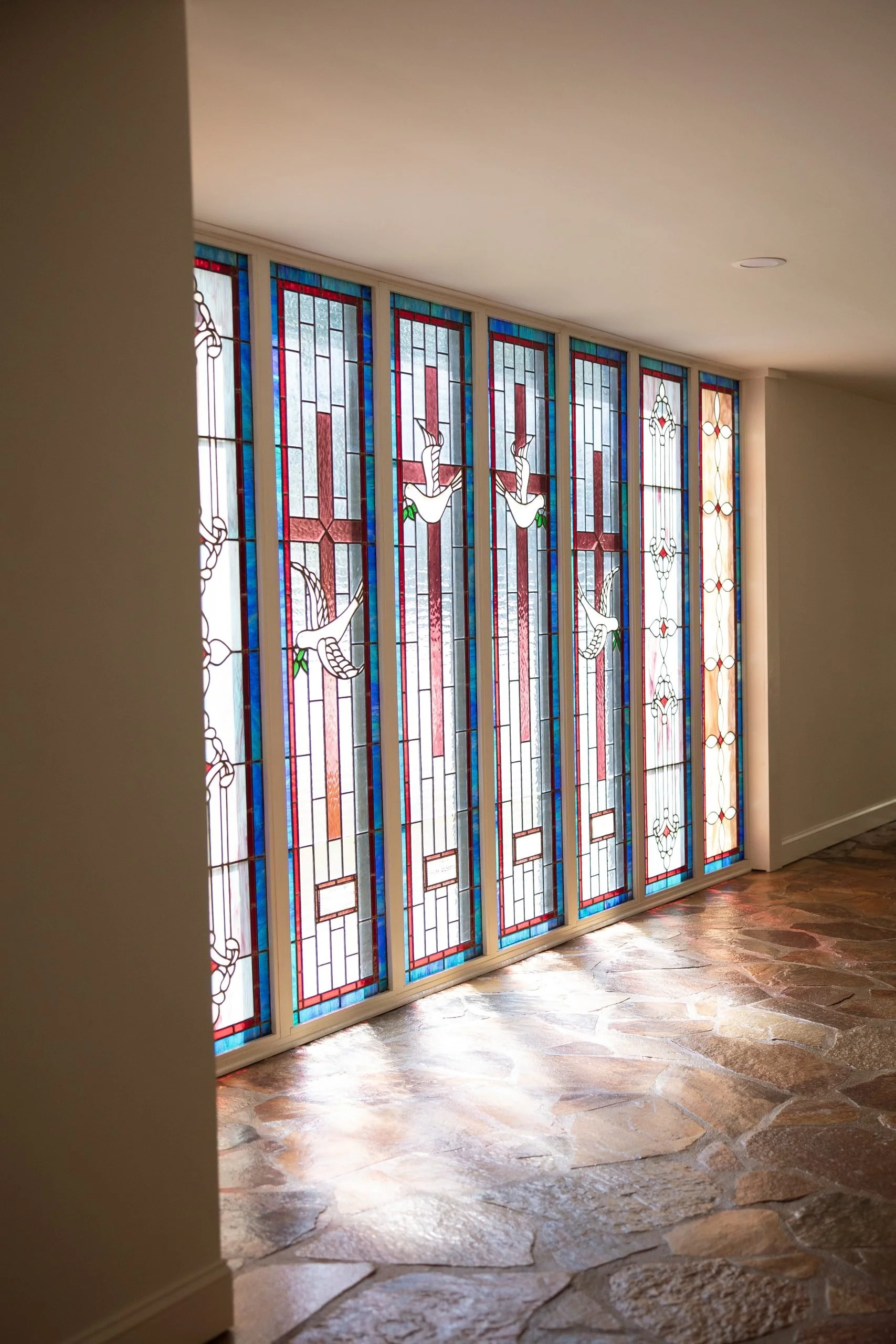 Colorful stained glass window with images of white doves, set in a white wall with a stone floor.