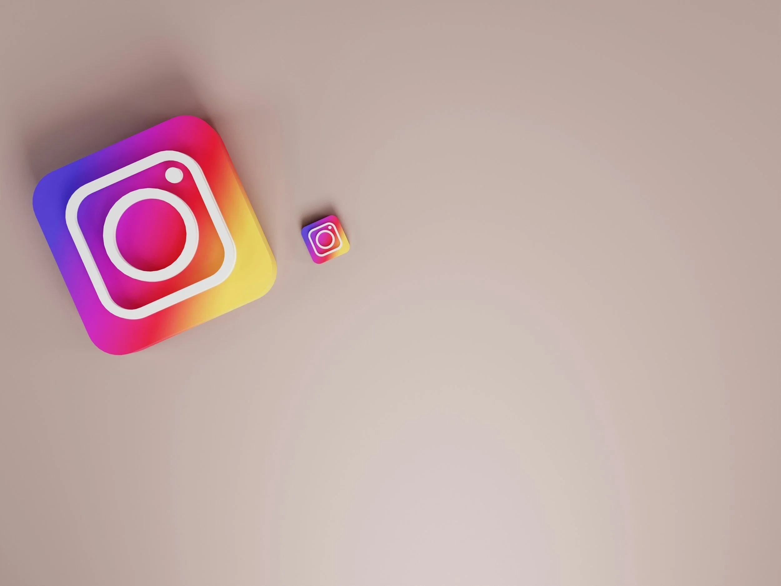 Close-up of two smartphone icons for Instagram on a beige surface, with the larger icon in the foreground and a smaller one in the background.