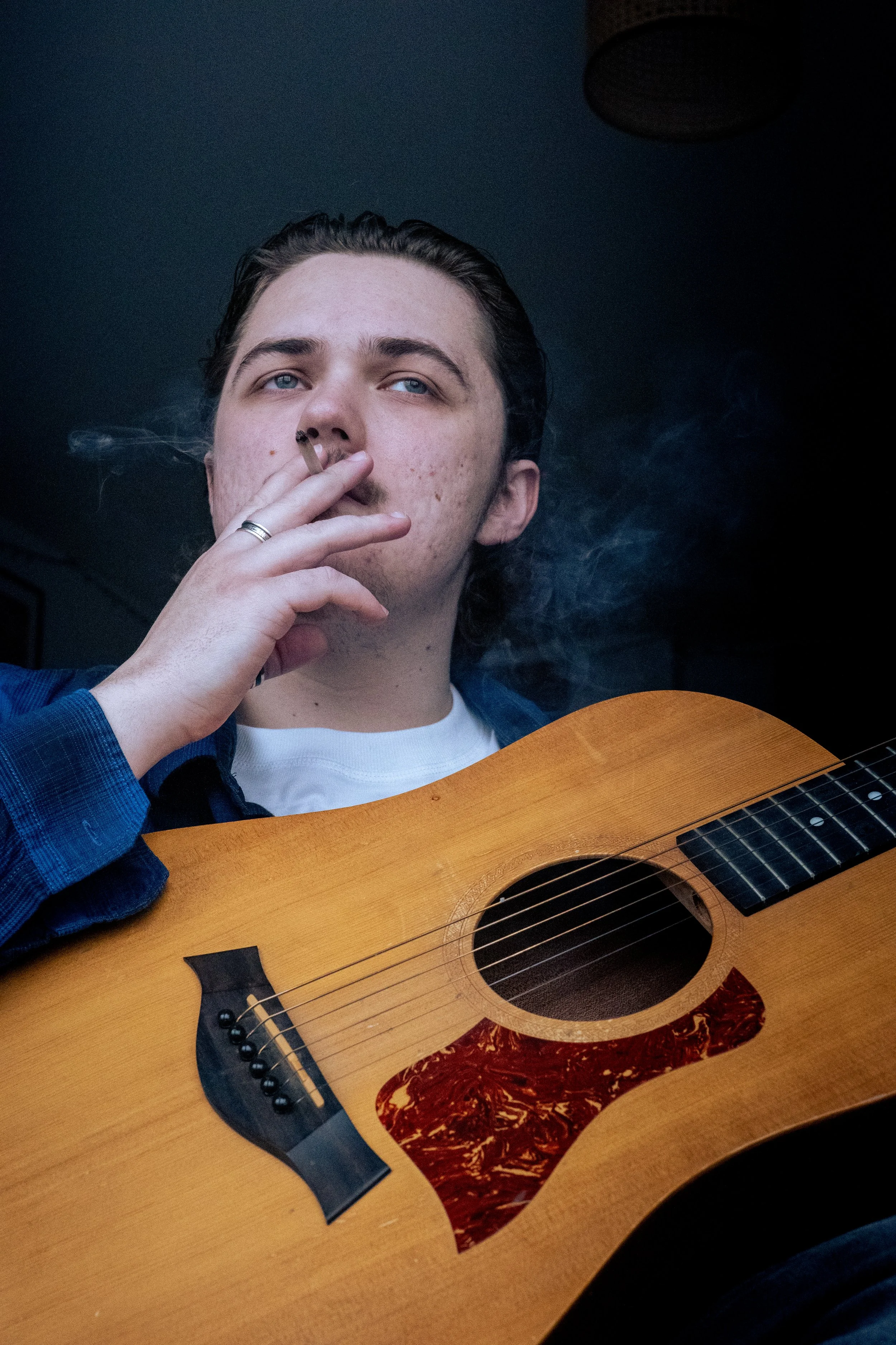 Young man smoking a cigarette and holding an acoustic guitar.