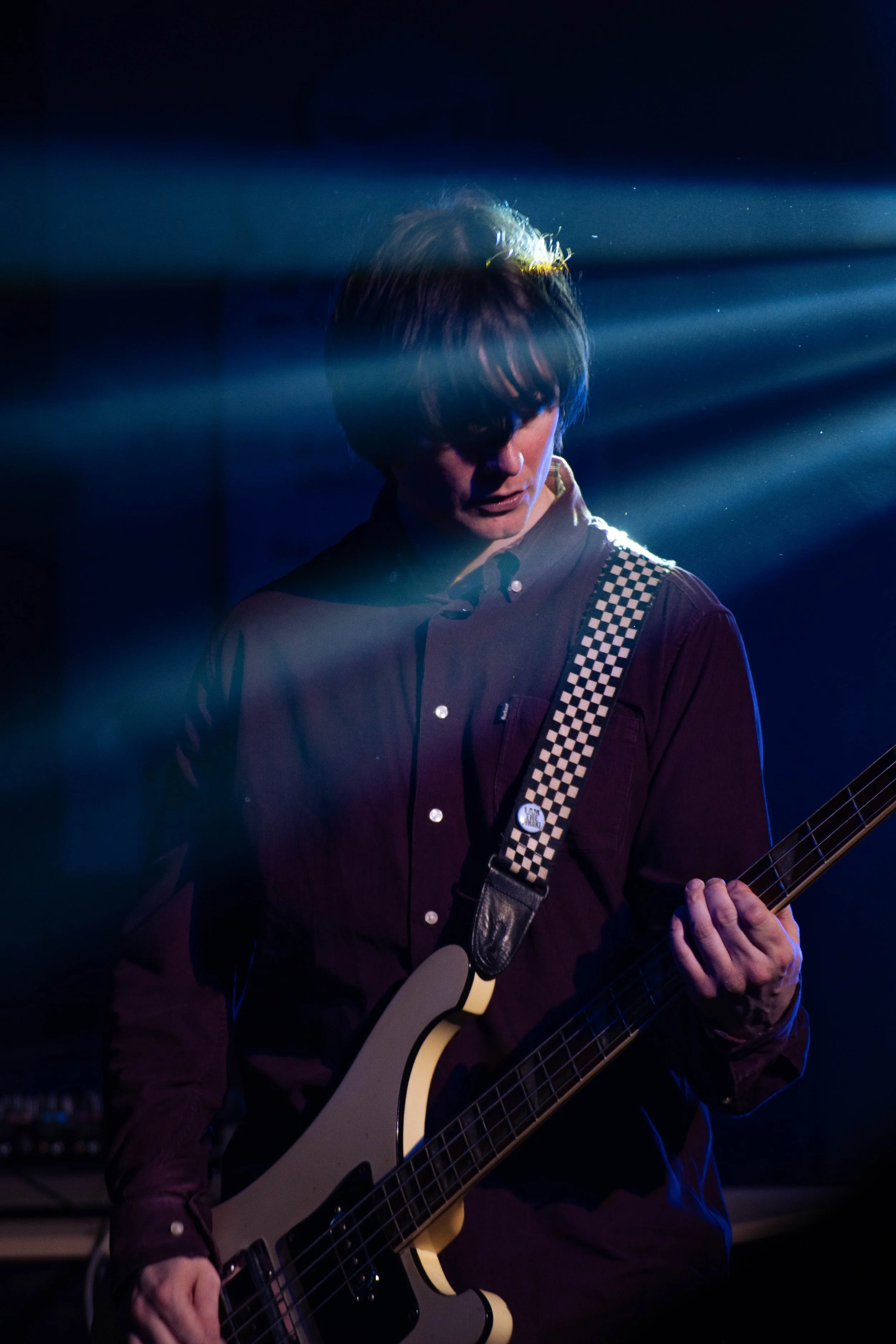 A musician playing an electric guitar on stage, with dramatic lighting and blue light beams across the scene.