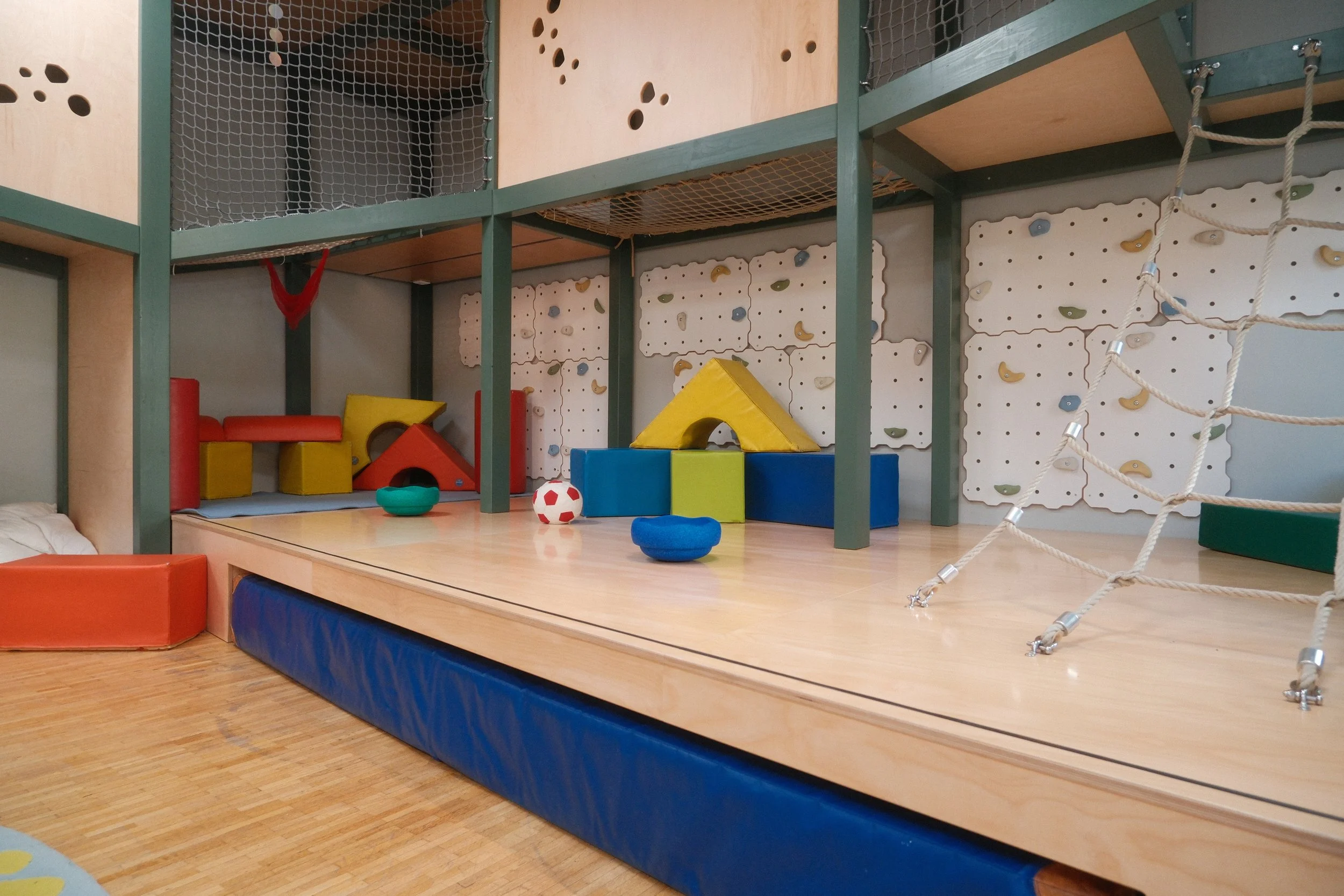 Foto vom Bewegungsraum mit Kletter- und Spielbereich für Kinder mit Boulderwänden, Stapelsteinen und Kletternetz