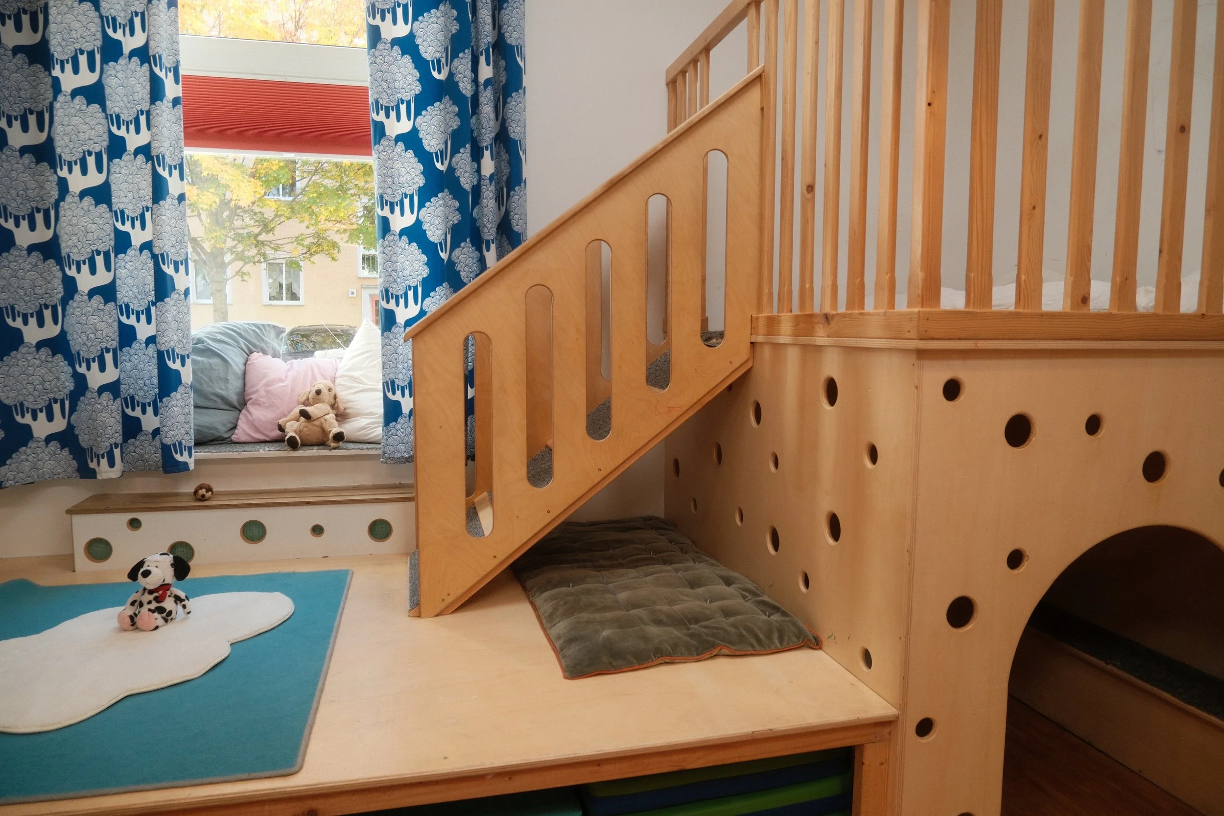 Foto vom Atelier mit Vorhängen mit Wolkenmuster und Holzspielturm mit eine Leiter.