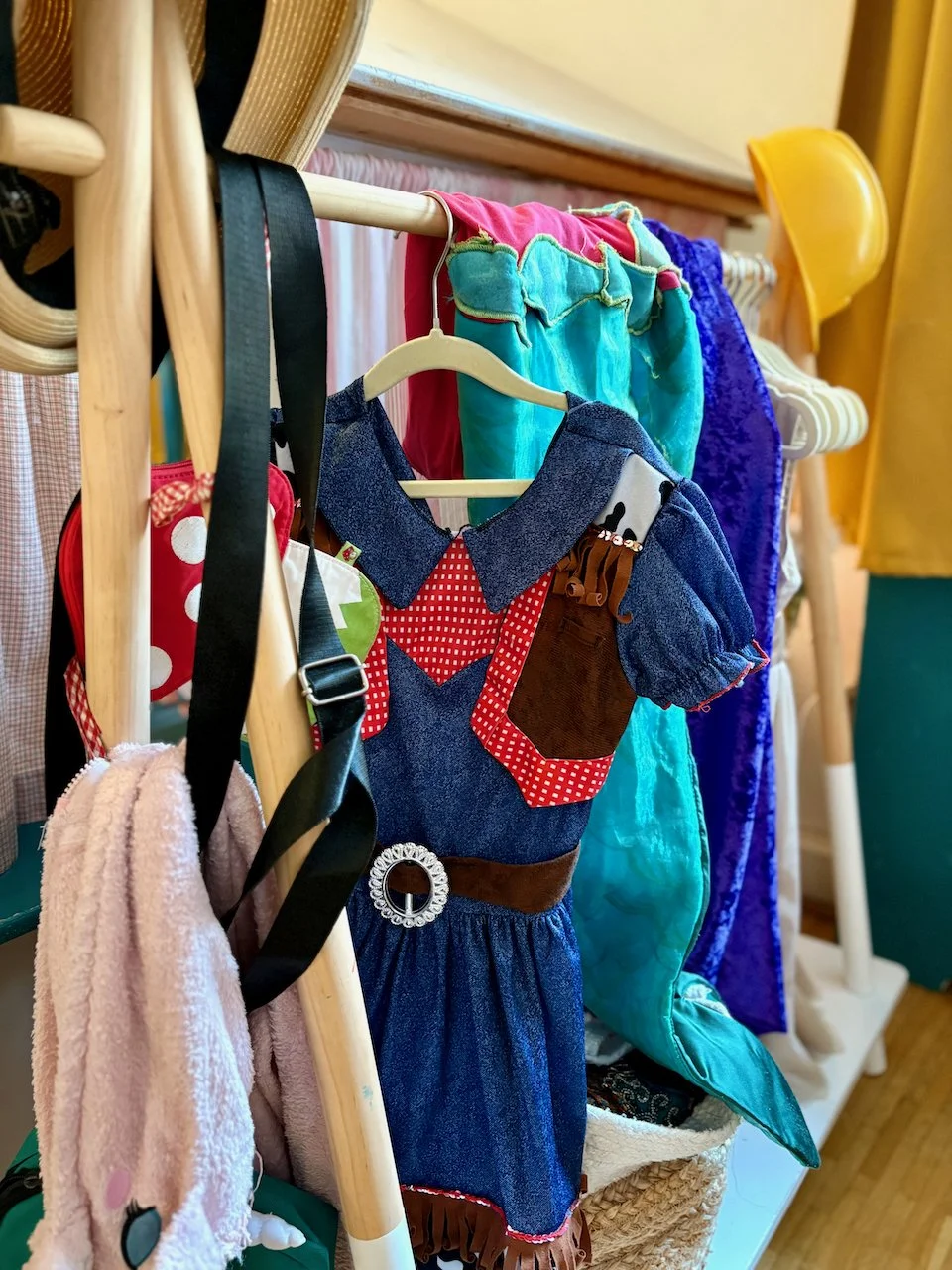 Foto Nahaufnahme von Kostümständer im Spielzimmer. Verschiedene bunte Kinderkleidung und Accessoires hängen an einem hölzernen Kleiderständer