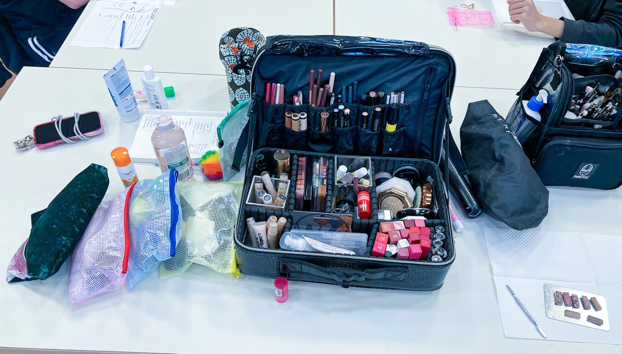 Matériel de maquillage organisé sur une table, comprenant différentes pochettes, pinceaux, rouges à lèvres, crèmes et autres produits cosmétiques.