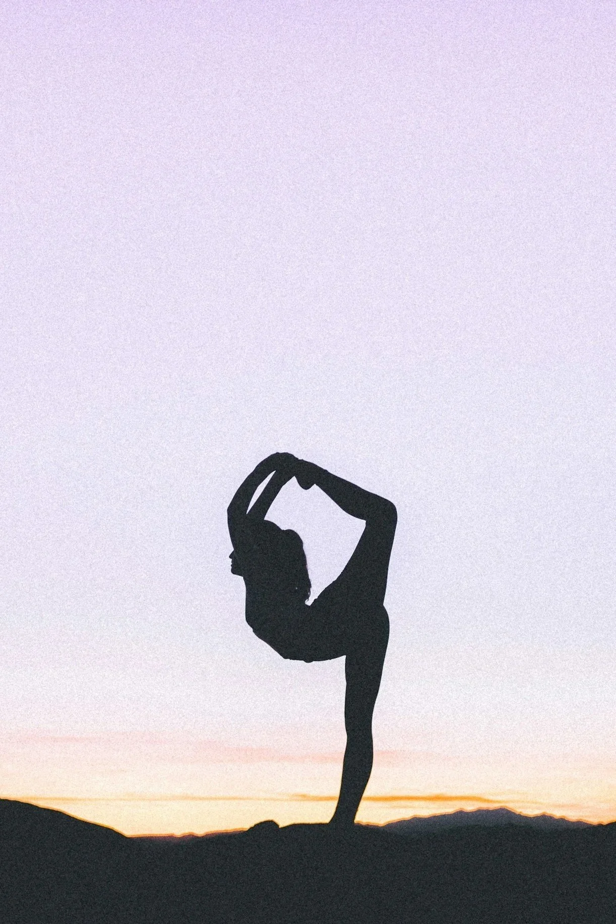 Silhouette d'une personne faisant un équilibre sur une jambe avec une posture de yoga ou de danse, contre un ciel pastel au coucher du soleil.