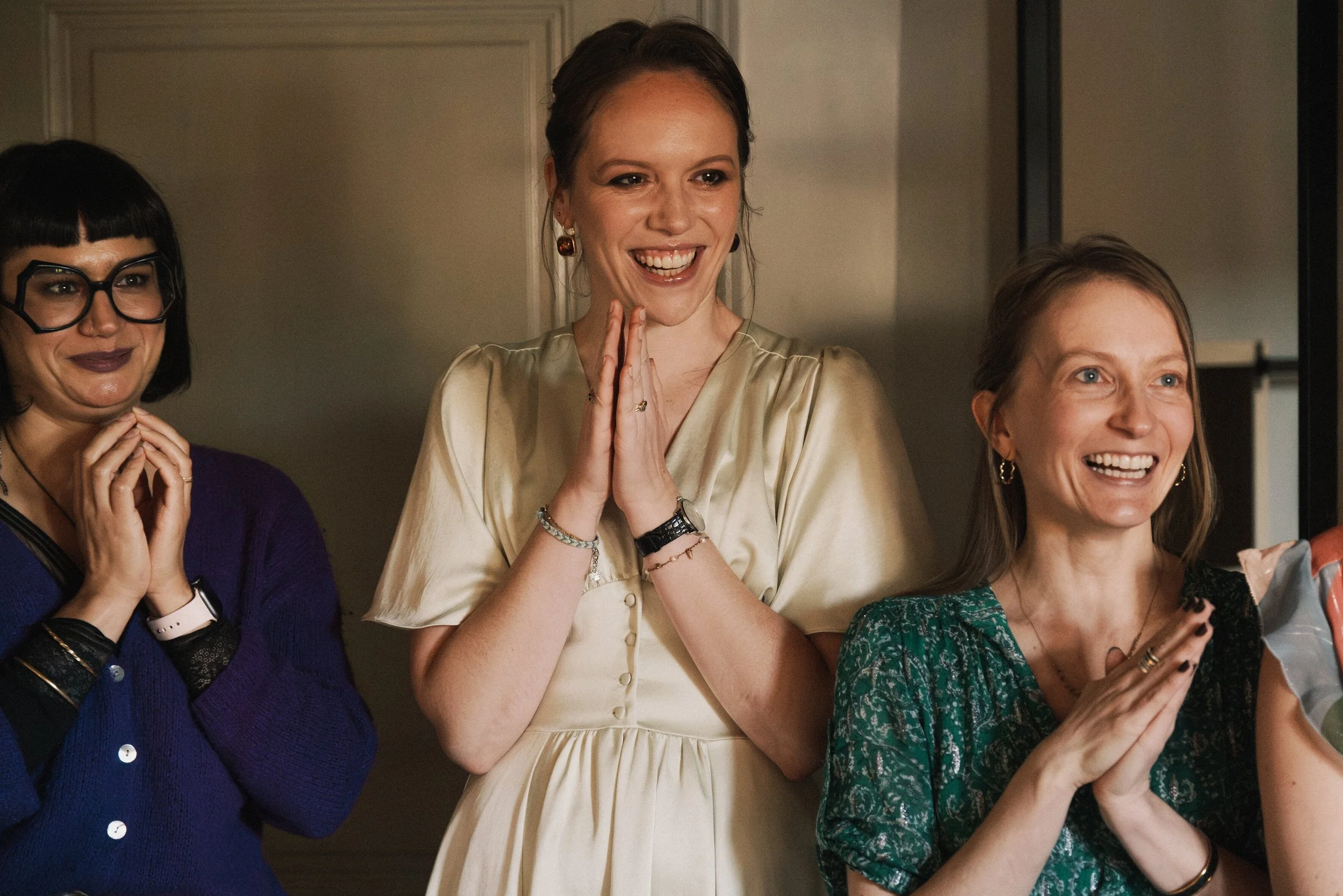 Trois femmes souriantes lors d'une célébration ou d'un événement social, applaudissant et partageant un moment joyeux.