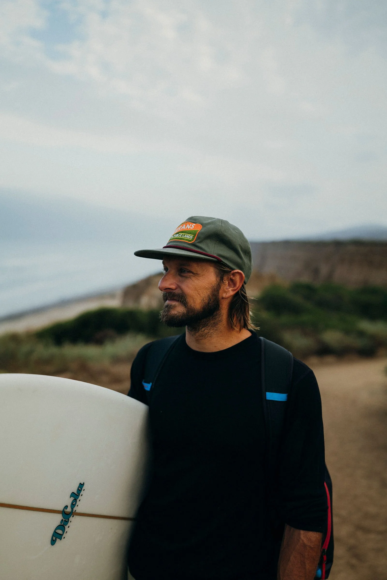 Nick in a cap holding a surfboard on the coast