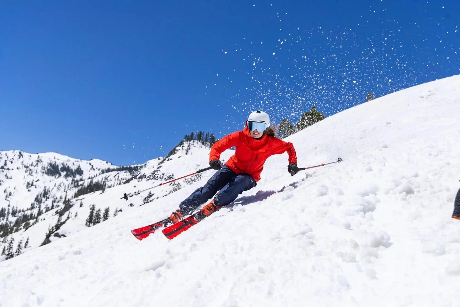 Skier in a red jacket carving down a snowy slope under a blue sky