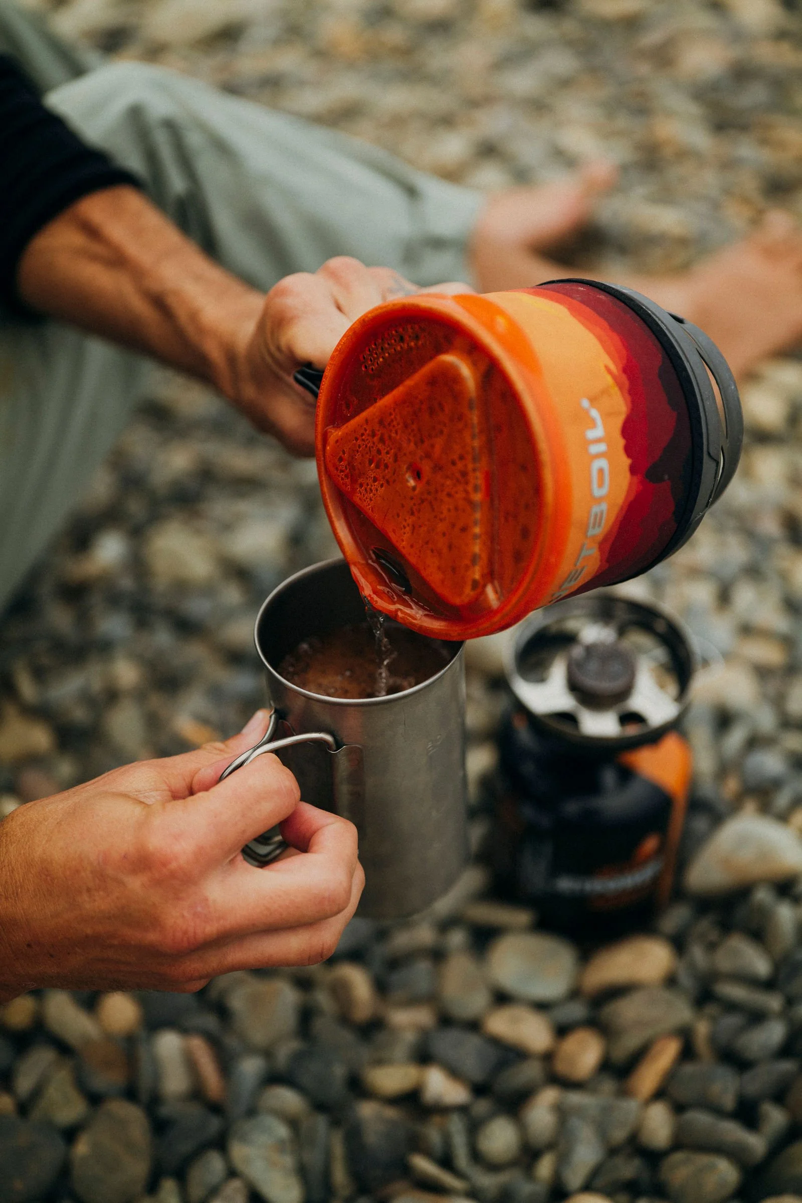 Pouring coffee from a camp stove on a rocky beach