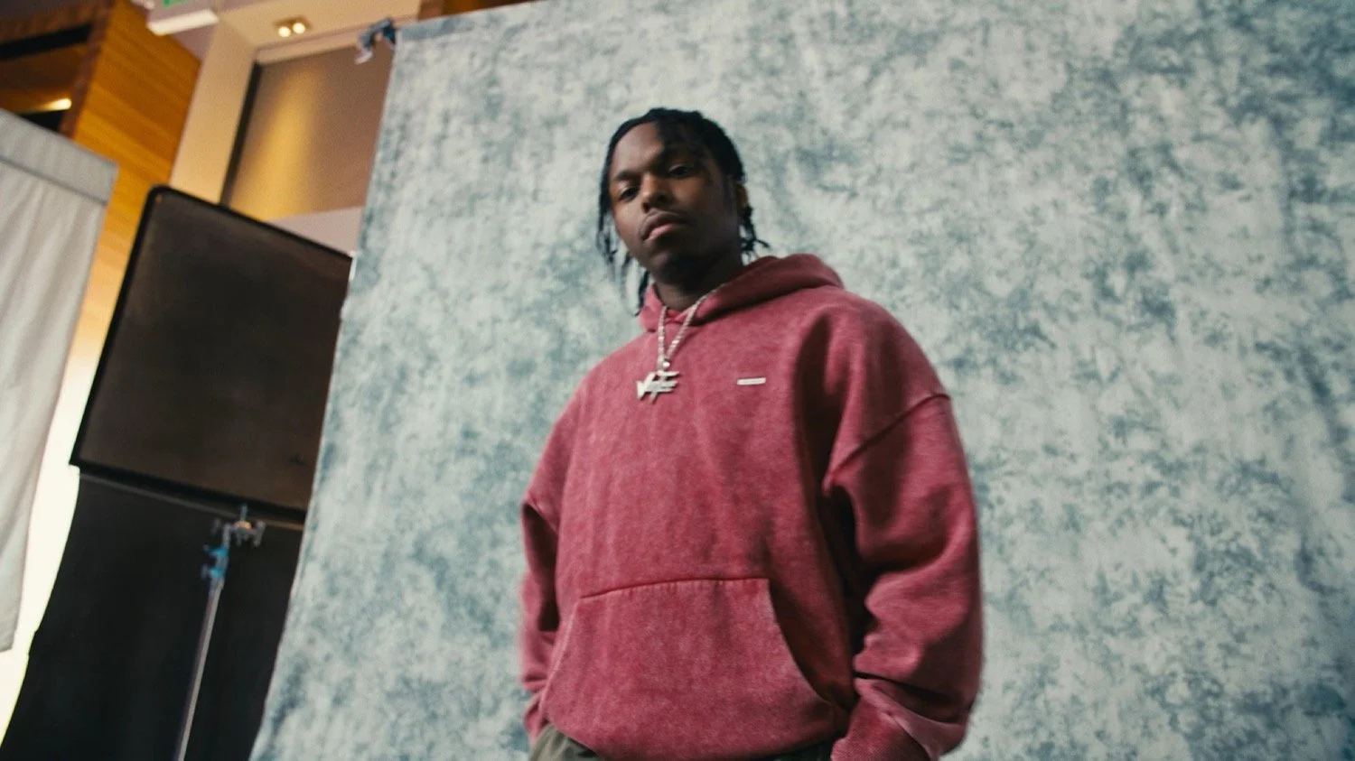 Young man in a red hoodie posing in front of a gray painted backdrop