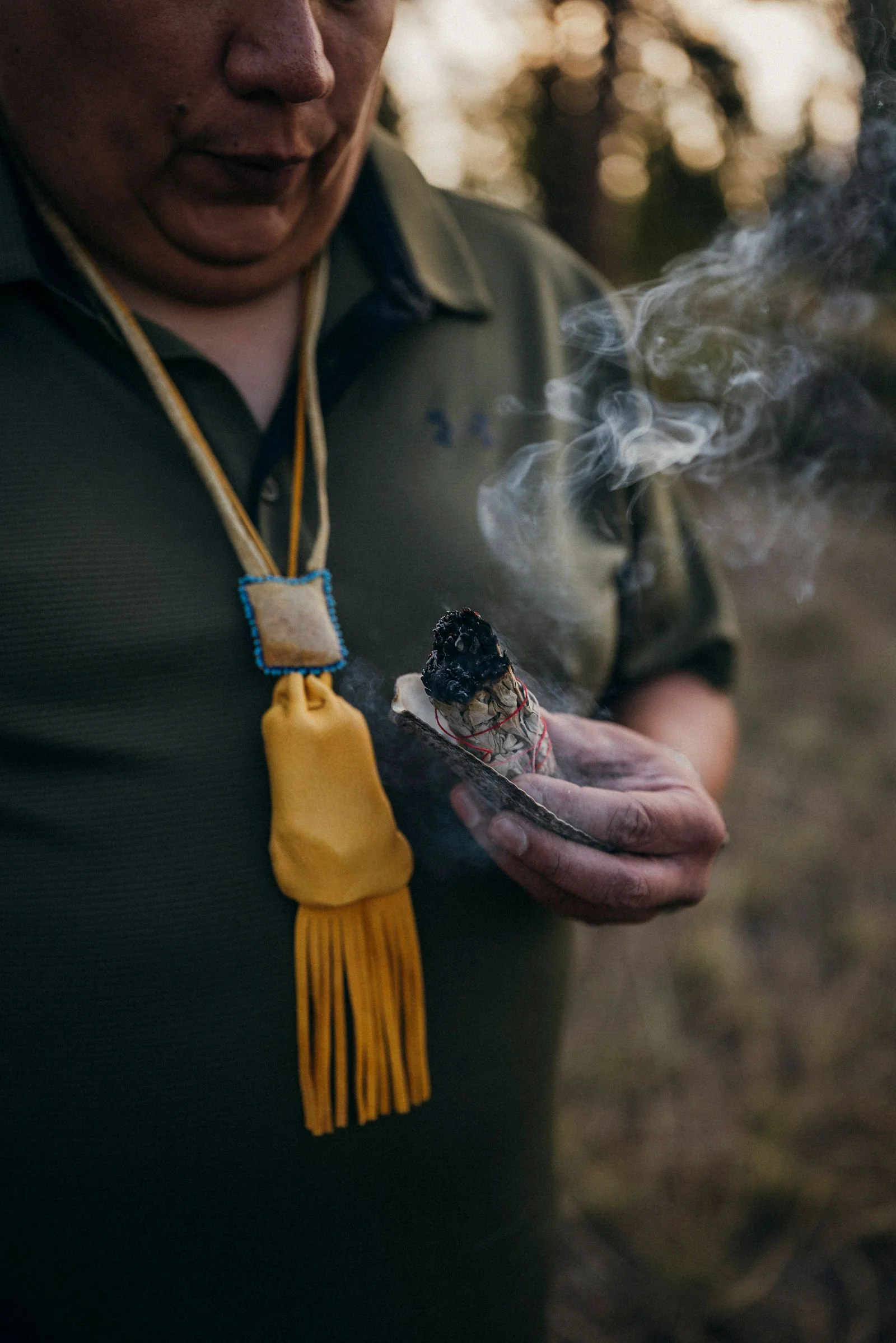Jonas holding burning sage, a beaded tassel necklace at his chest