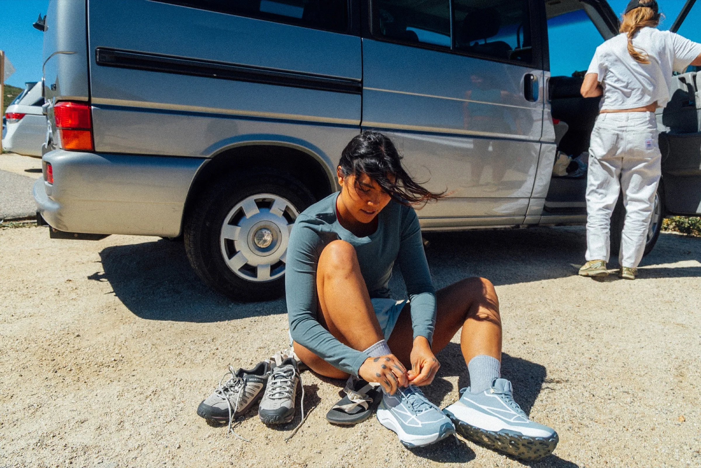 Woman lacing up her running shoes beside a parked van