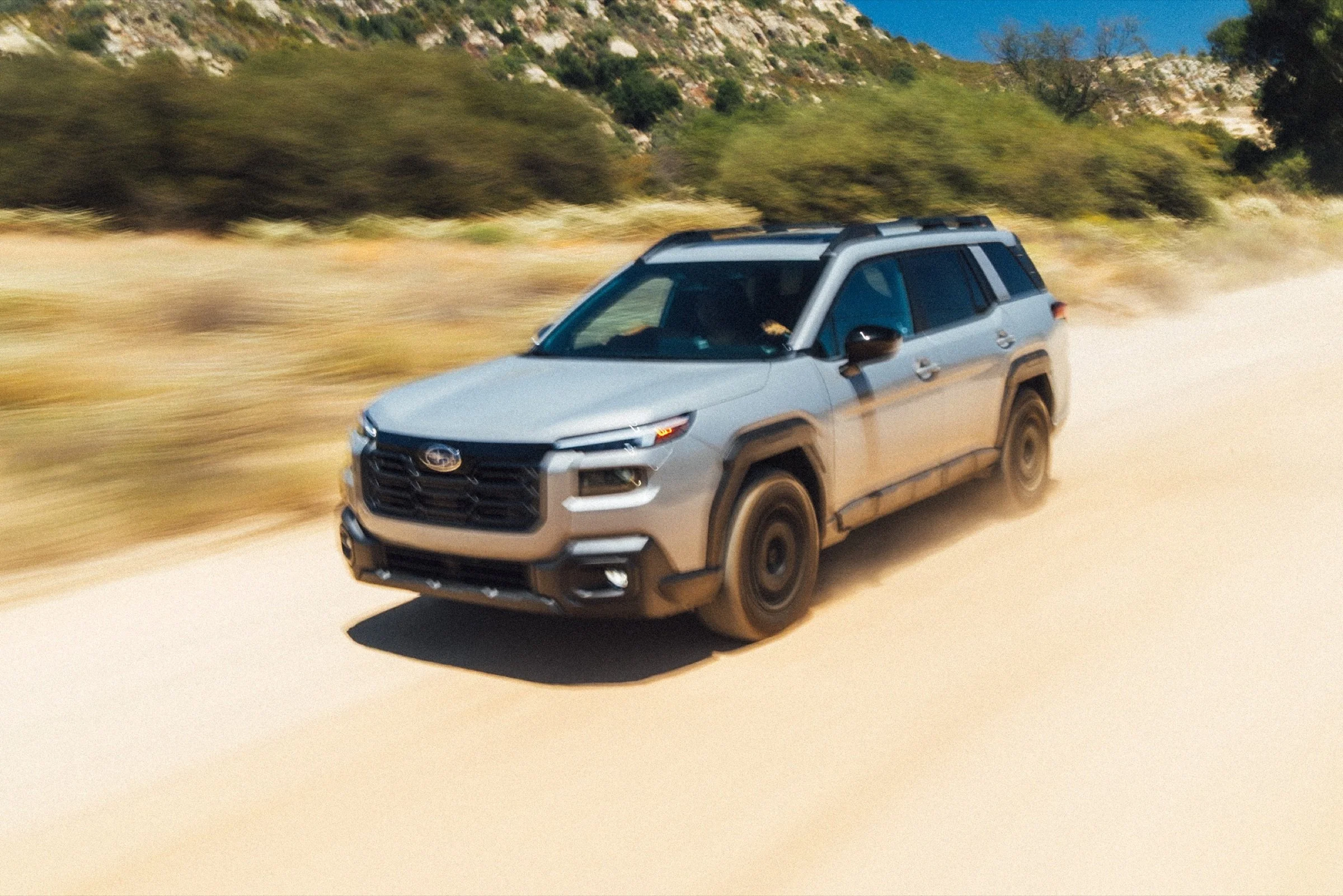 Subaru Outback kicking up dust on a desert dirt road