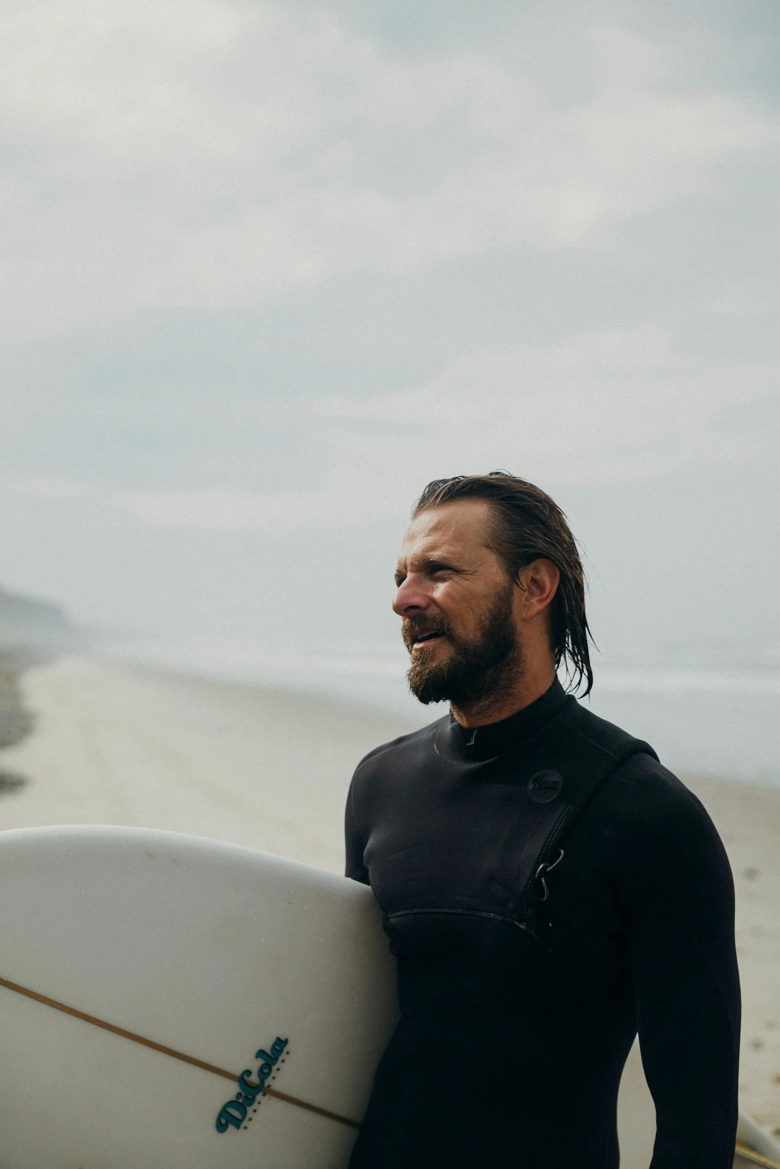 Nick in a wetsuit holding a surfboard, looking out to sea