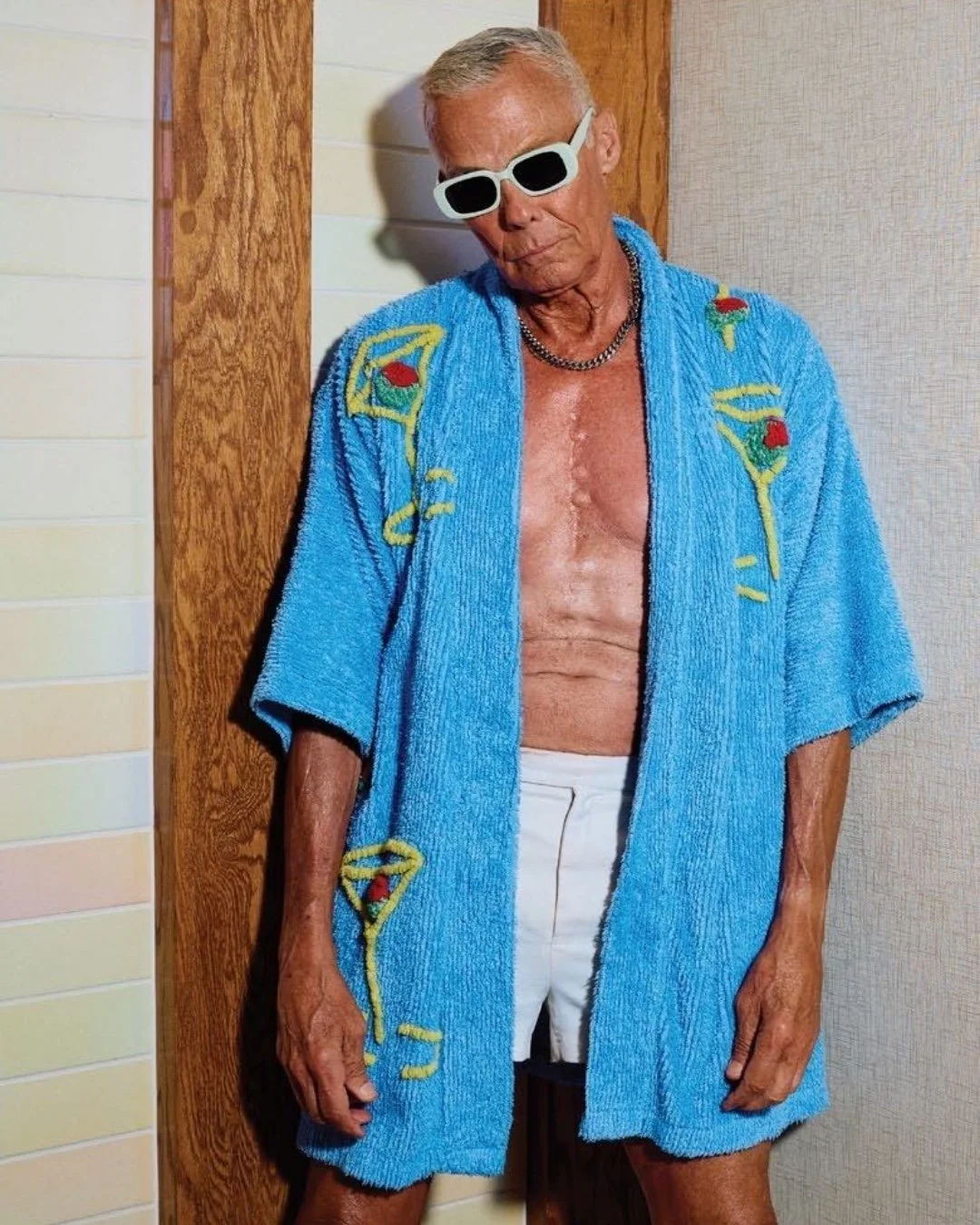 Older man in white sunglasses and an open blue robe embroidered with cocktails
